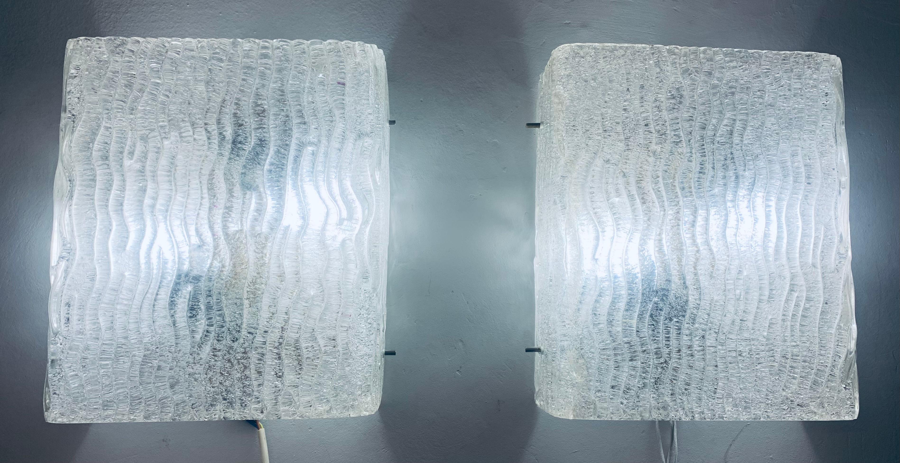 Pair of large 1960s wall lights or wall sconces designed by J.T. Kalmar and manufactured by Kalmar Lighting in Vienna, Austria. The heavy sculpted, textured, molded glass has a vertical wave pattern covering its entire outside surface which produces