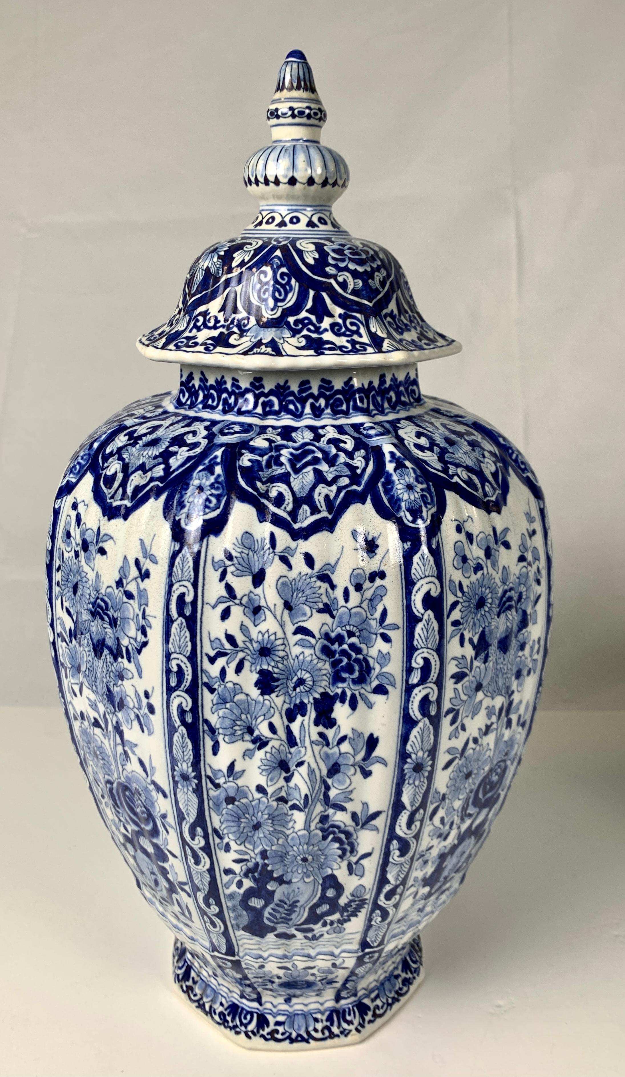 This pair of large Delft jars have a traditional blue chinoiserie decoration of flowers painted on a white tin-glaze ground. 
Each jar has six panels showing beautiful flowers flowing from rockwork.
The shoulders and cover are decorated with deep