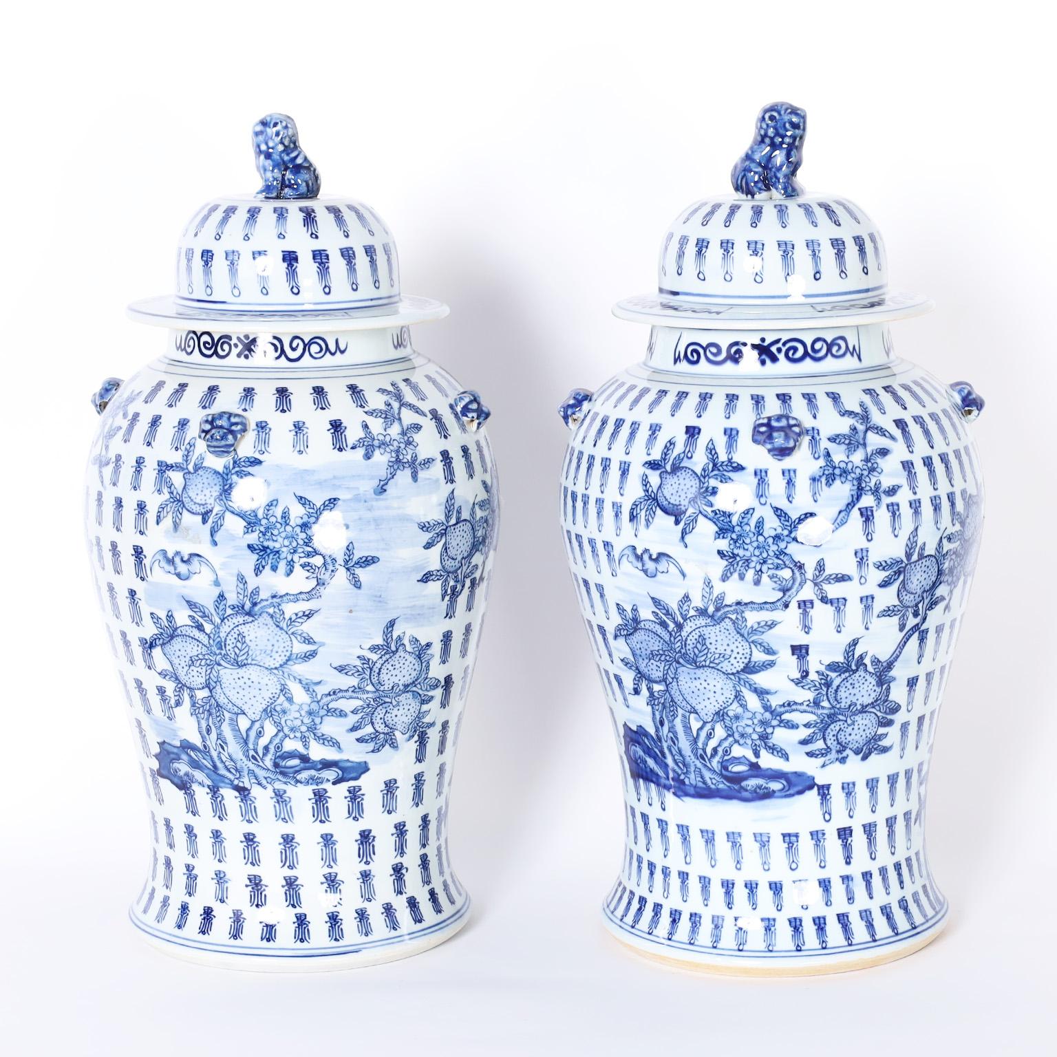 Pair of Chinese blue and white porcelain lidded urns with classic form featuring foo dog handles on top and hand decorated with an auspicious composition of fruit trees and birds in a field of repeating characters.