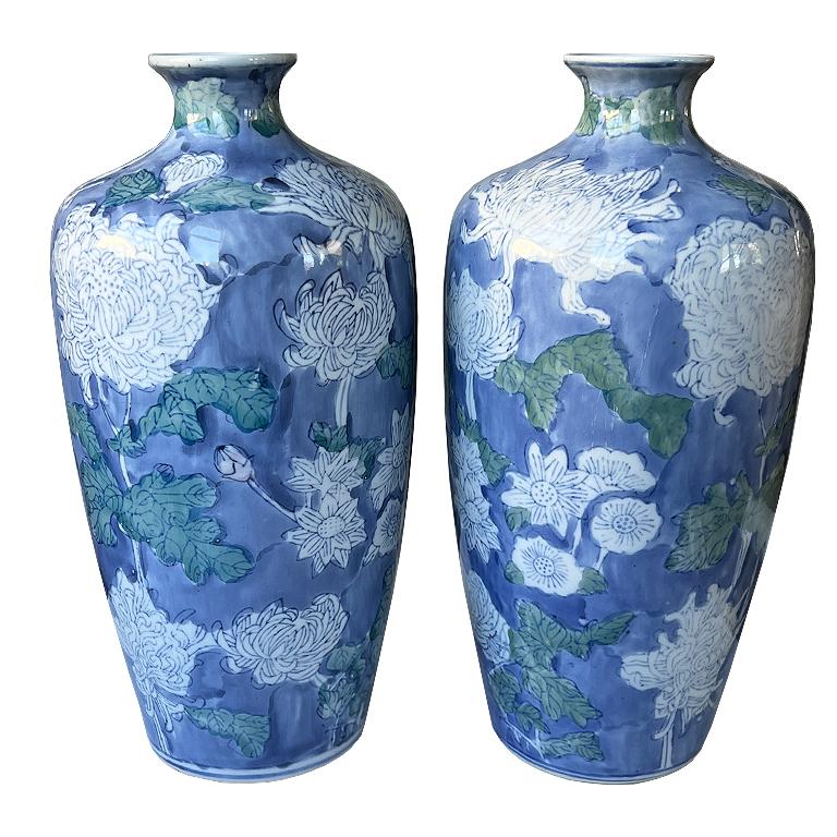 A pair of timeless ceramic vintage blue and white floral vases. This set comes as a pair and will elevate any space. A classic expression of Asian artistry and sophisticated floral design. Featuring hand-painted white chrysanthemums, peonies, and
