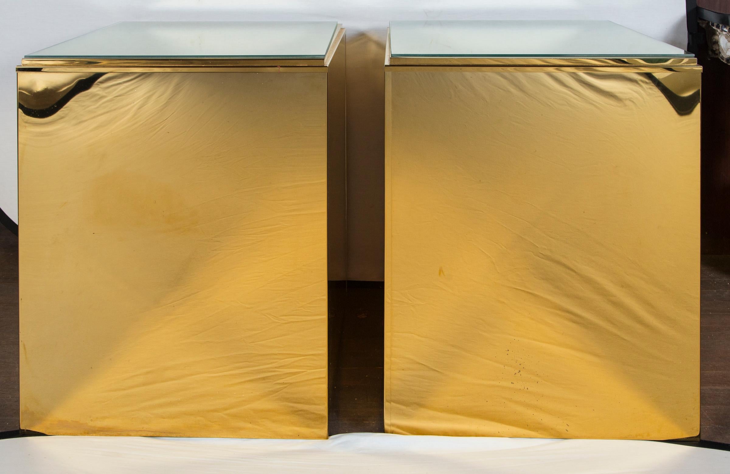 A pair of sleek brass cube pedestals or side tables with additional protective glass tops. Useful as sofa end tables or as pedestals for a pair of sculptures or objects. The brass is in excellent condition.
