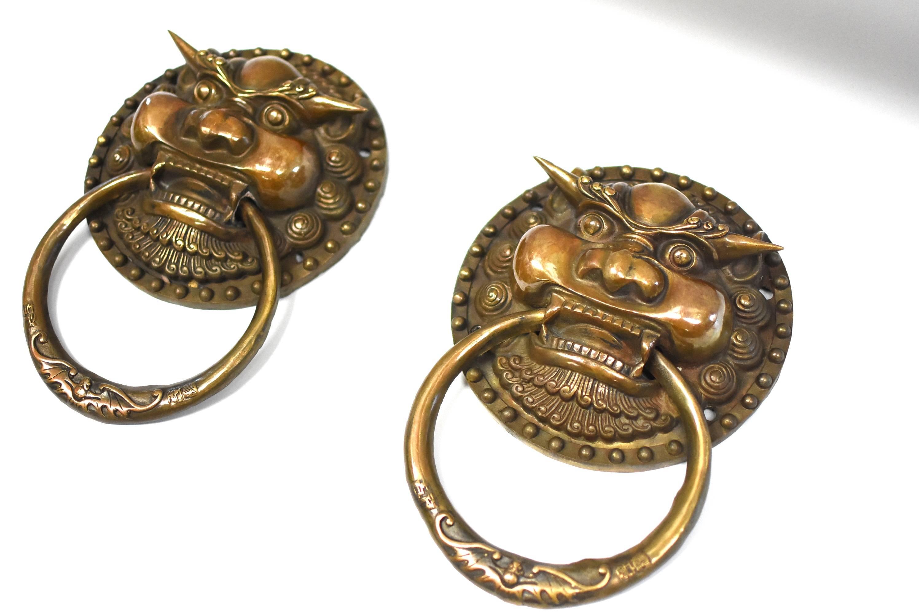 A pair of beautiful bronze dragon motif knockers. The mythical dragon has large bulging eyes under sharp thick eyebrows. Heavy cheekbones echoes the prominent forehead, highlighting his masculine feature. A wide open mouth above double mustaches.