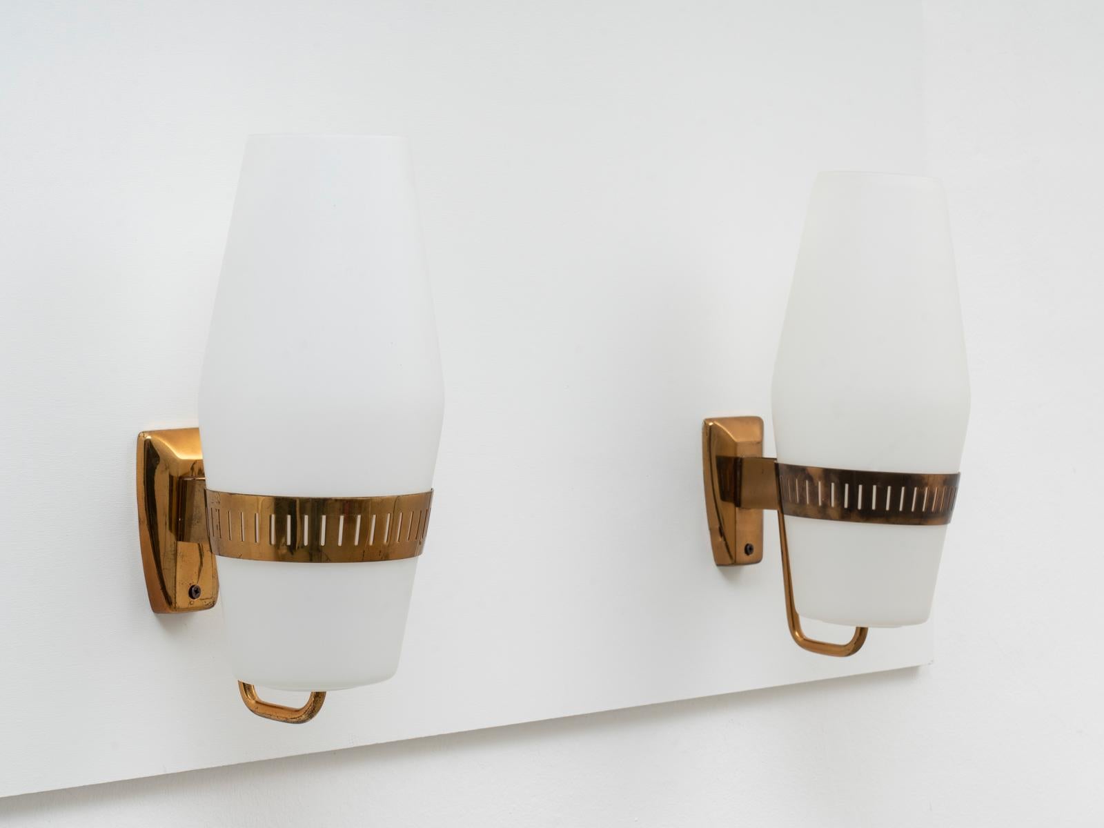 This pair of wall sconces was manufactured by Stilnovo in 1959 and no longer in production since decades. The model is documented as n. 2078. They are made of a solid brass structure and triplex-opaline glass shades. Both sconces are stamped