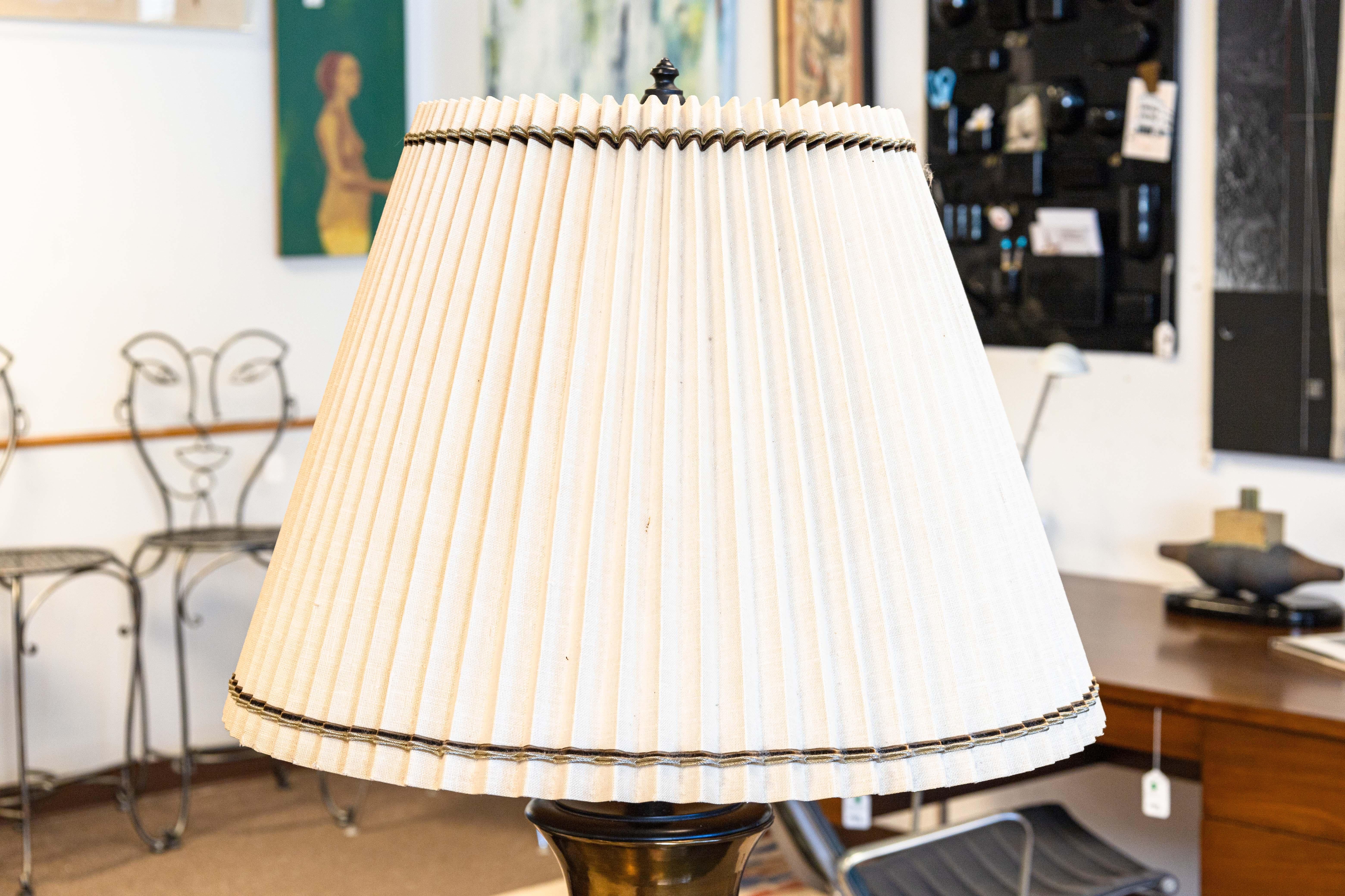 A pair of large brass mid century modern table lamps. These beautiful vintage lamps feature a brass finish with a domed shape. The bases feature a black wood, and the shades are a pleated fabric with an accented fabric on the top and bottom of the