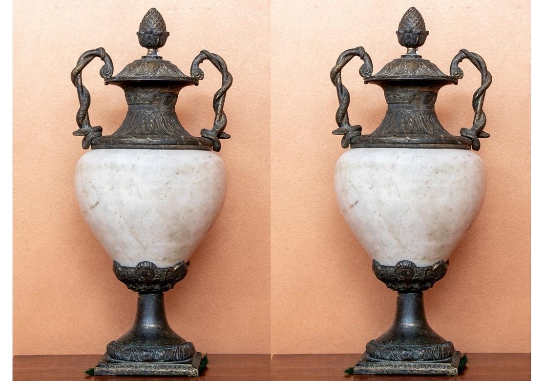Finely crafted large white and brown marble urns with patinated bronze mounts. The lids with artichoke finials, palmettes and acanthus leaves, attached to the necks decorated with leaves. With pairs of twisted snake handles. The bulbous marble urns
