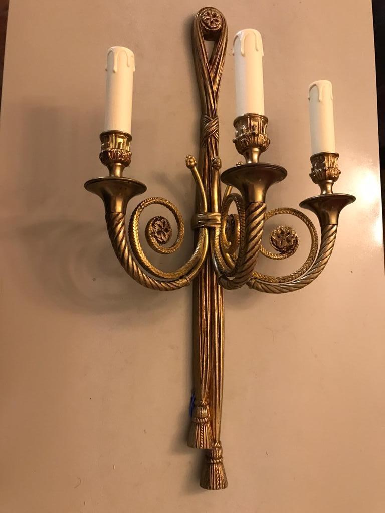Large pair of sconces in gilt bronze. The scroll detailing on the arms is a detailed acanthus  style. The bound crossover of the two arms and the fabulous tassels are wonderful details. Circa 1940s.