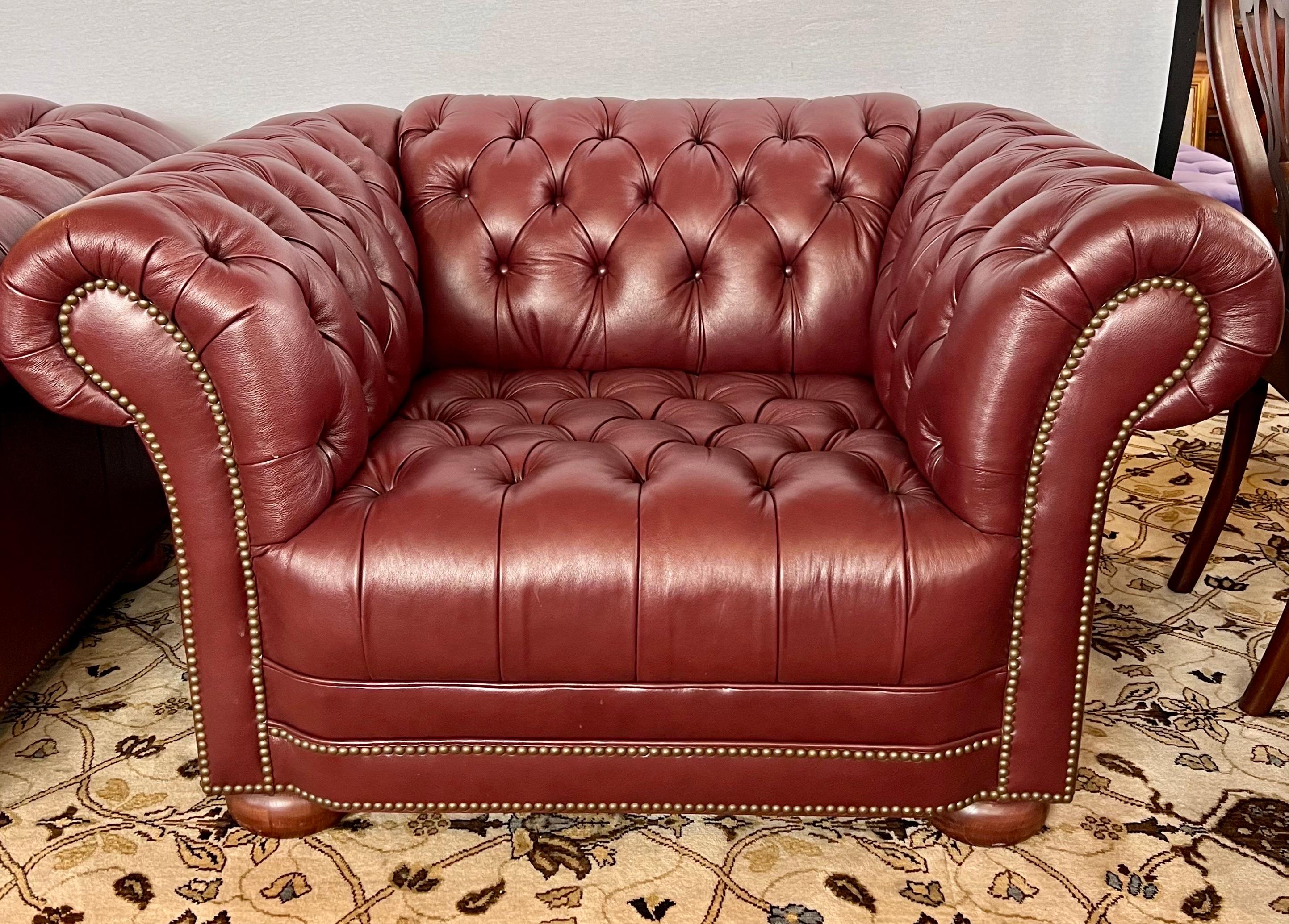 Handsome, handcrafted in the USA, burgundy button tufted leather chesterfield club chairs in excellent condition. Features an extra wide and deep seat. Finished with brass nailhead trim and scrolled arms and raised on mahogany bun feet. Button