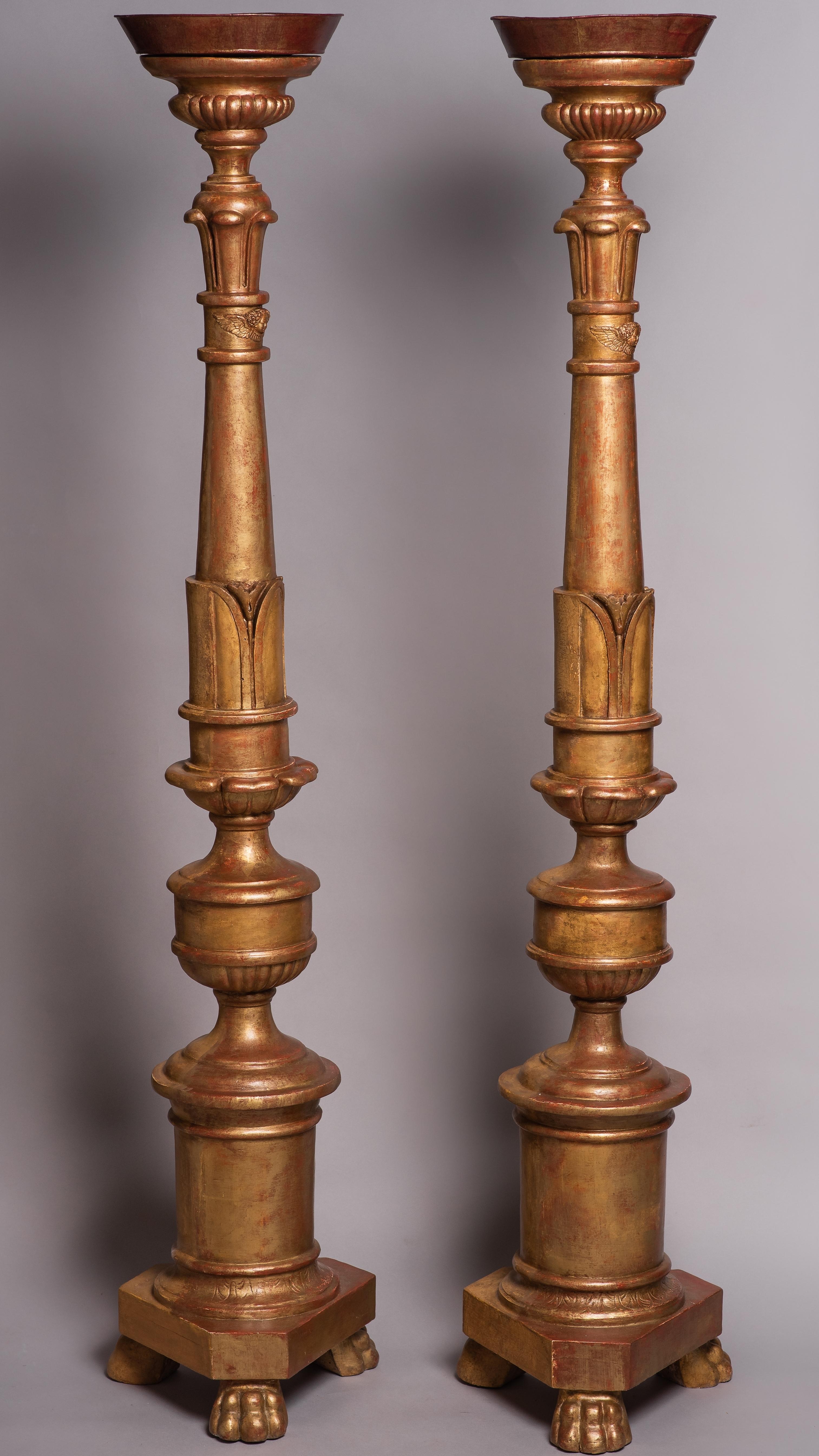 Two large candelabra-candlesticksdecorated with lion claw and cherub heads on the on the visible side .
They are turned wood and are decorated, engraved and gilded only on one side because they were intended to be presented in a corner of a chapel.