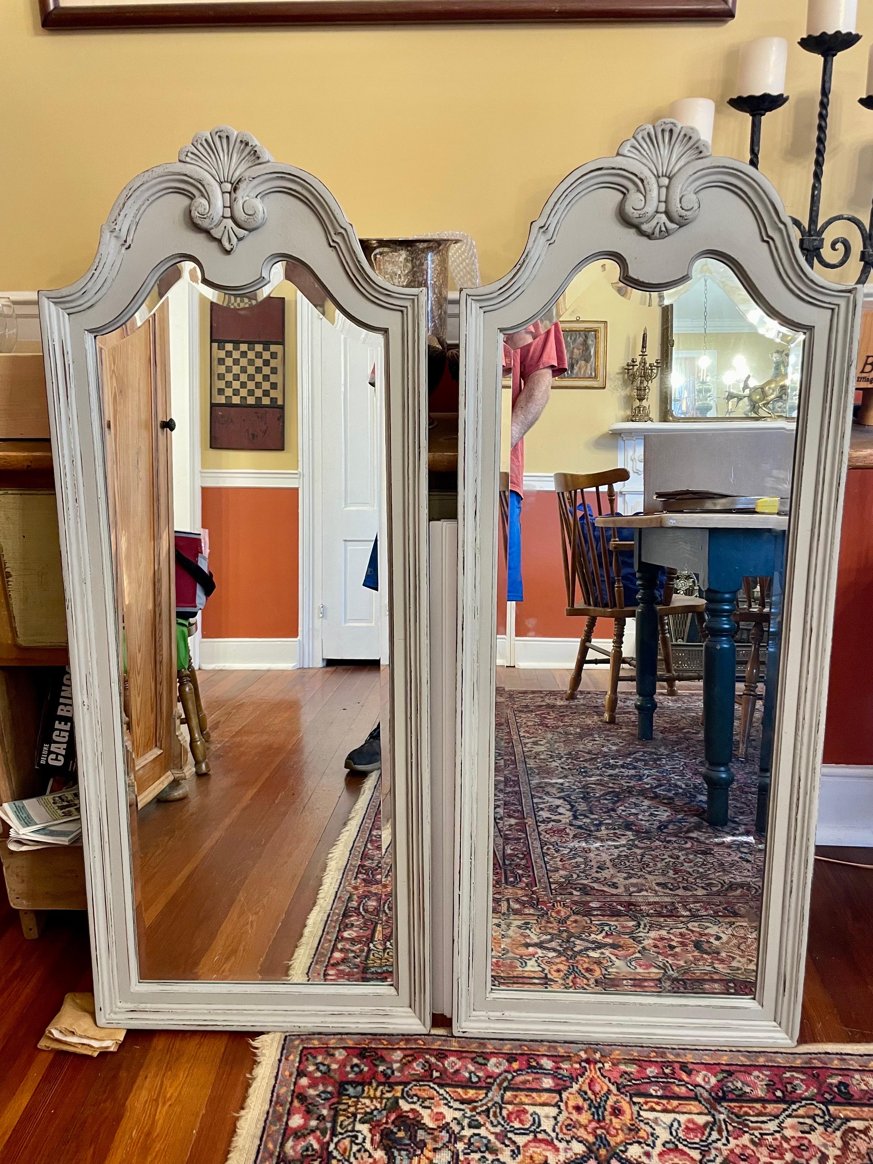 Pair of large carved painted beveled Hollywood Regency mirrors with grey painted distressed finish. Large scale. Some wear to finish from age and use. 1970's, painted more recently. Great detail highlighted by distressed finish.