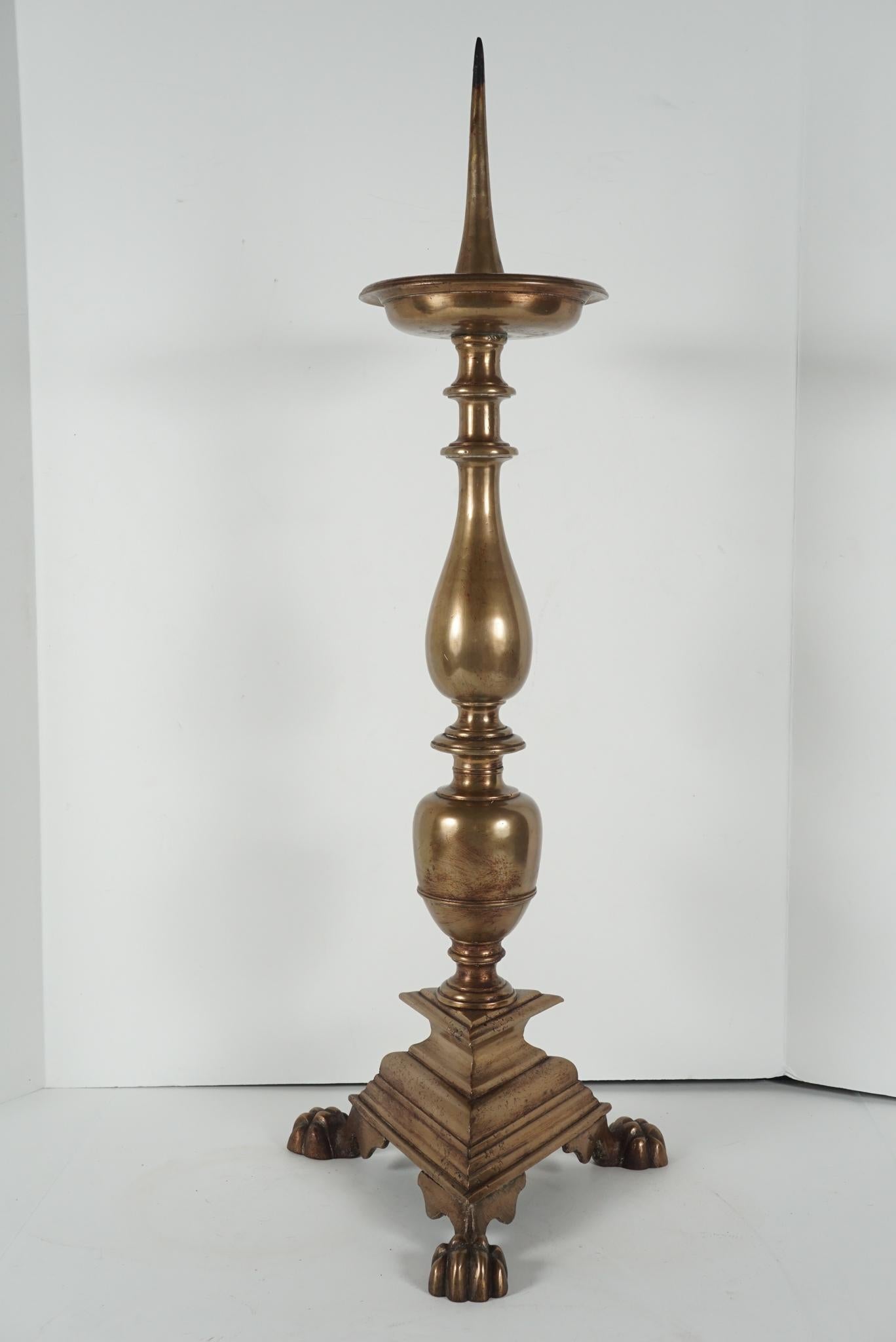 This large pair of heavily cast bronze pricket candlesticks were made circa 1780-1800. Designed as a tall balustered and egg knopped shaft resting on a triangular base set with lion paw feet. The pair has an old but well-loved surface patina showing