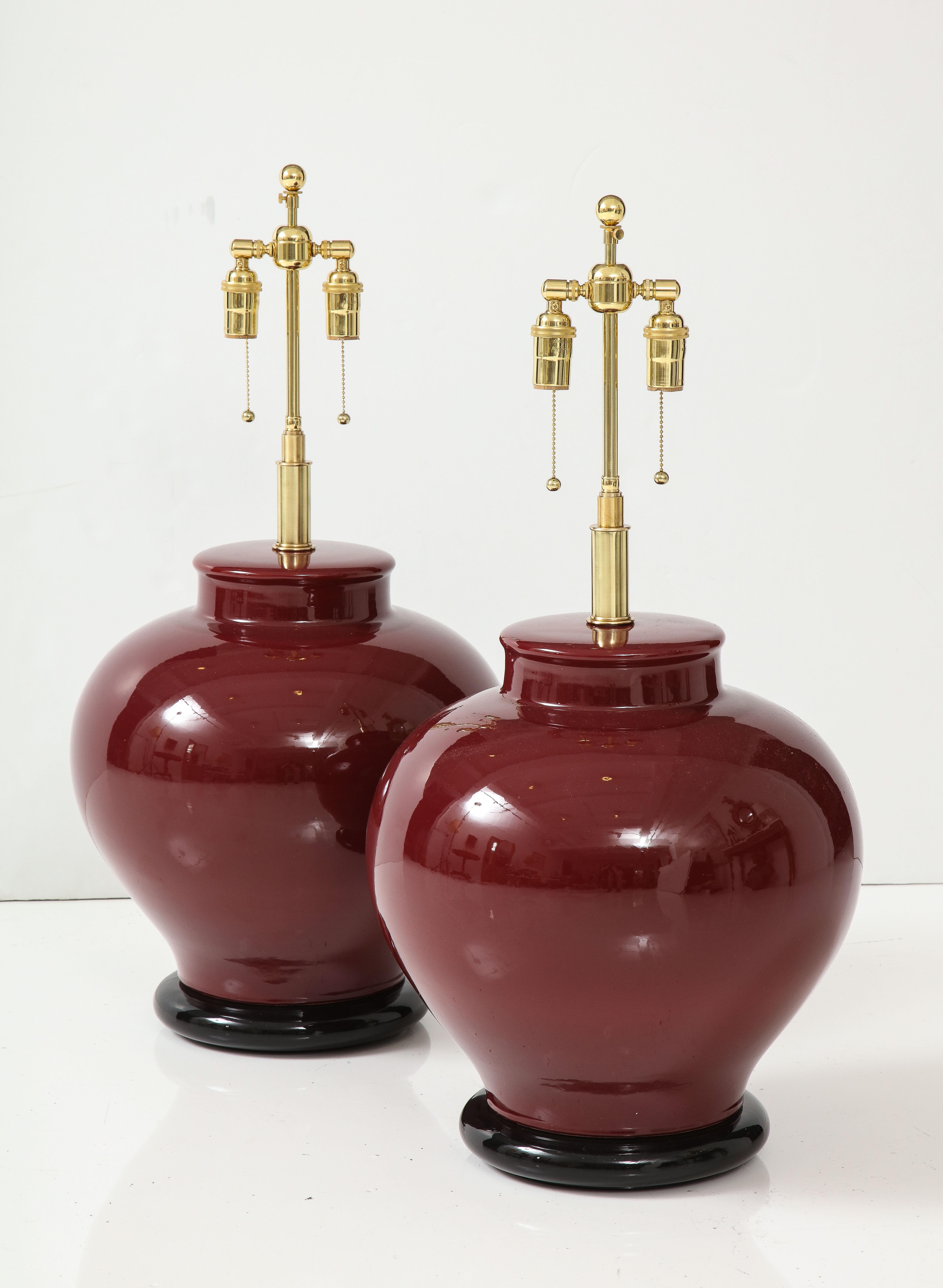 Pair of large ceramic lamps with a Rich Burgundy glaze finish.
The lamps are mounted on Black lacquered bases and have been Newly rewired with adjustable polished brass double clusters that take standard size light bulbs and silk rayon cords.
The