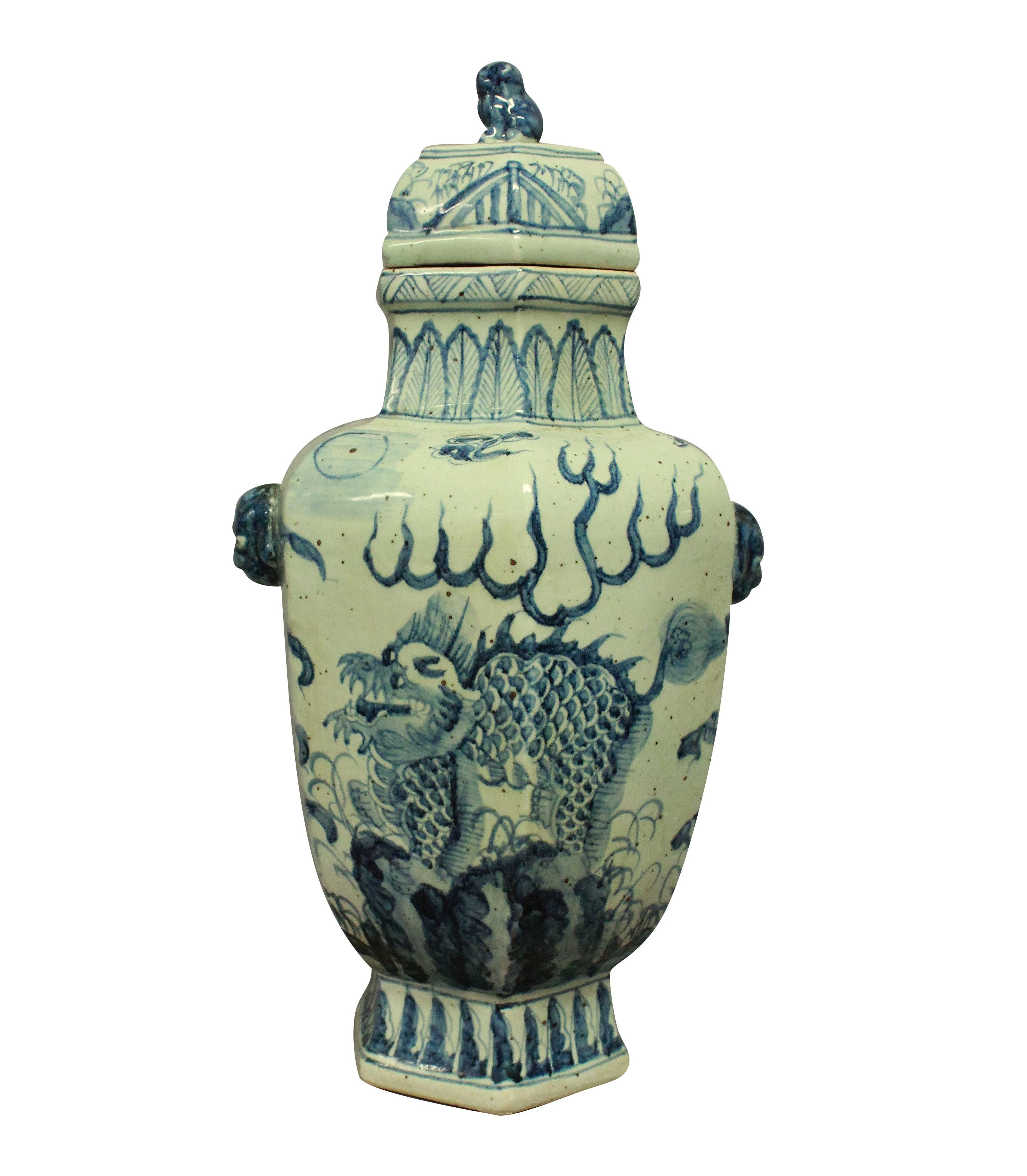 Une paire de grands vases chinois bleus et blancs peints à la main avec couvercles. De forme hexagonale bulbeuse, chacune représentant des dragons et les couvercles avec des épis de faîtage en forme de chien.