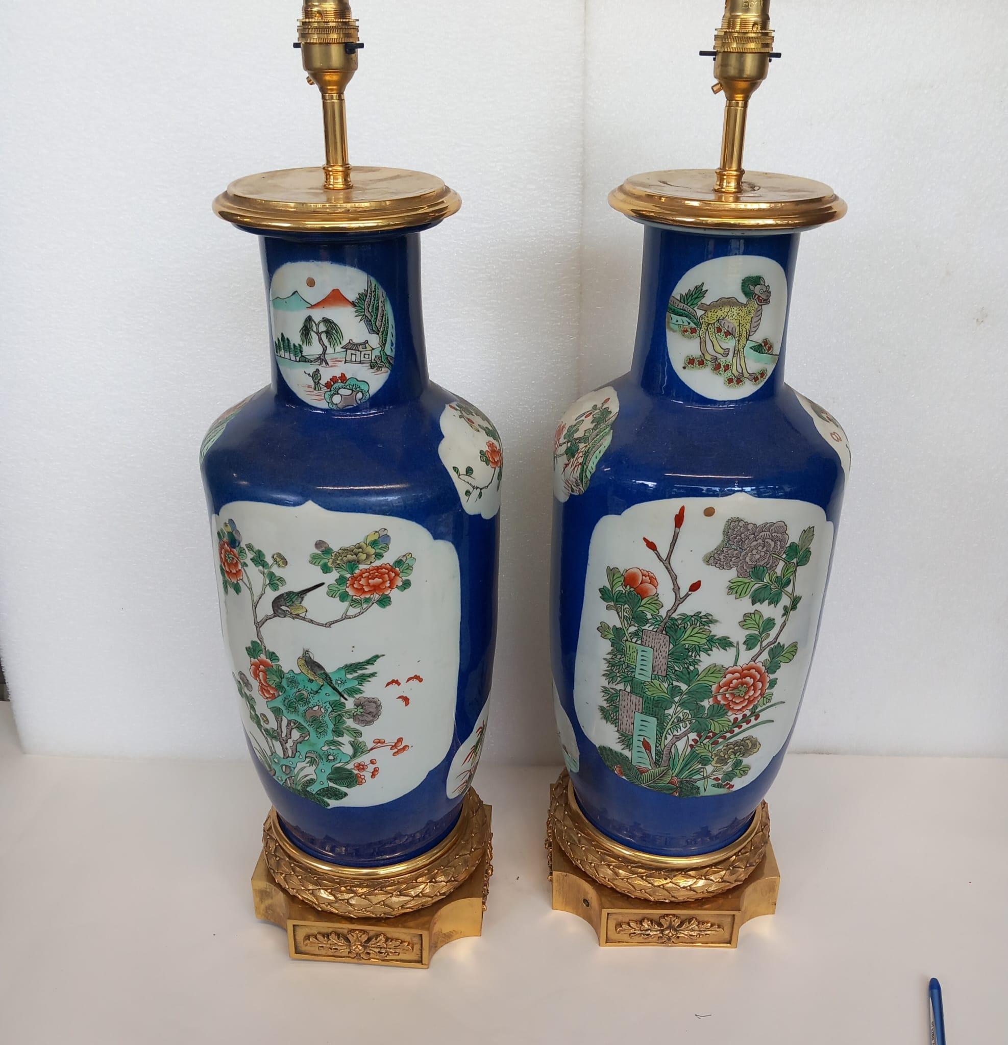 Pair of large Chinese blue vases , mid to late nineteenth century, converted into lamps, with enamel decorations of birds courting among flowering shrubs. The base of the vases resting on a gilt bronze stand, with laurel leaf designs. The tops have