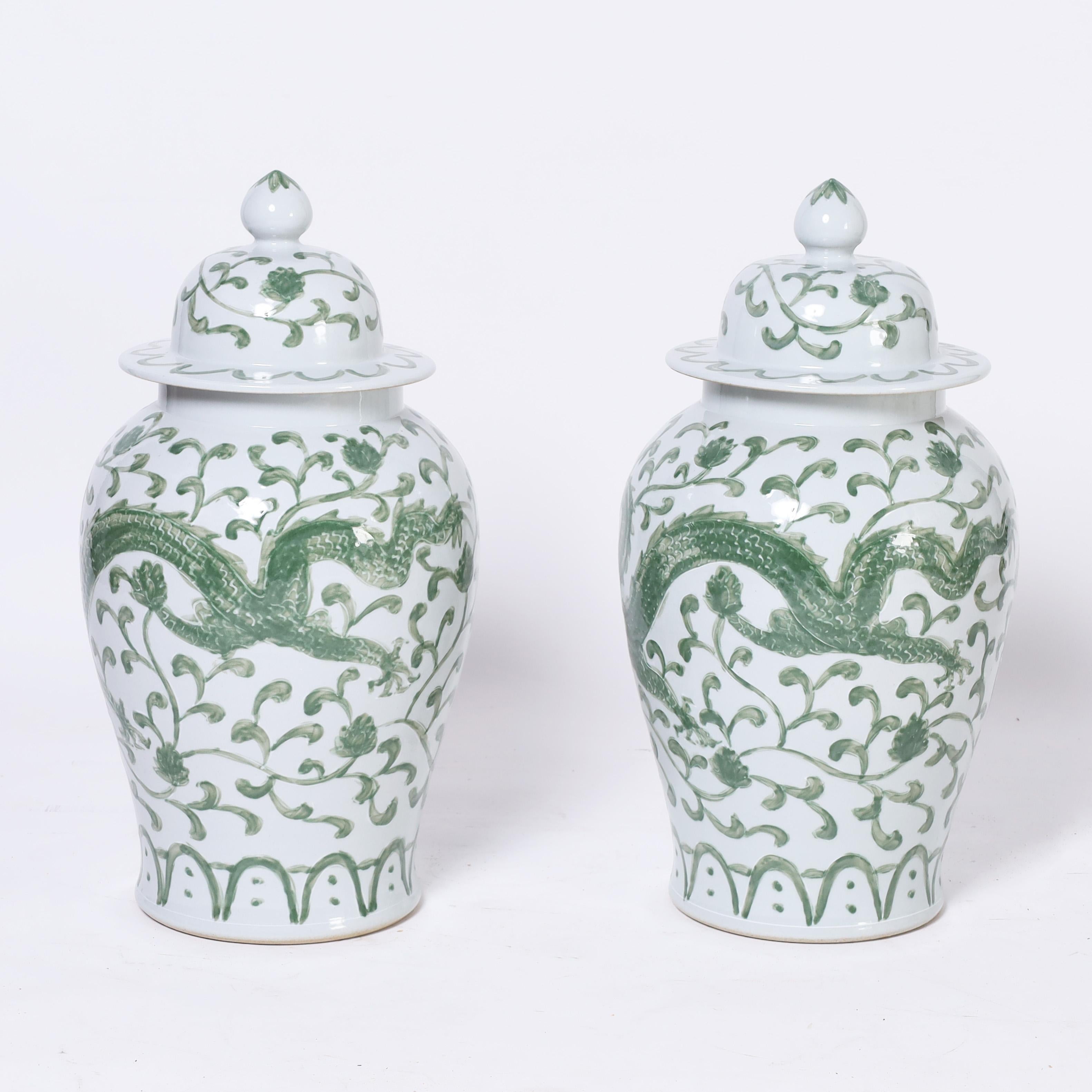 Striking pair of Chinese porcelain lidded jars handcrafted in classic form and hand decorated with dragons in a floral field. 