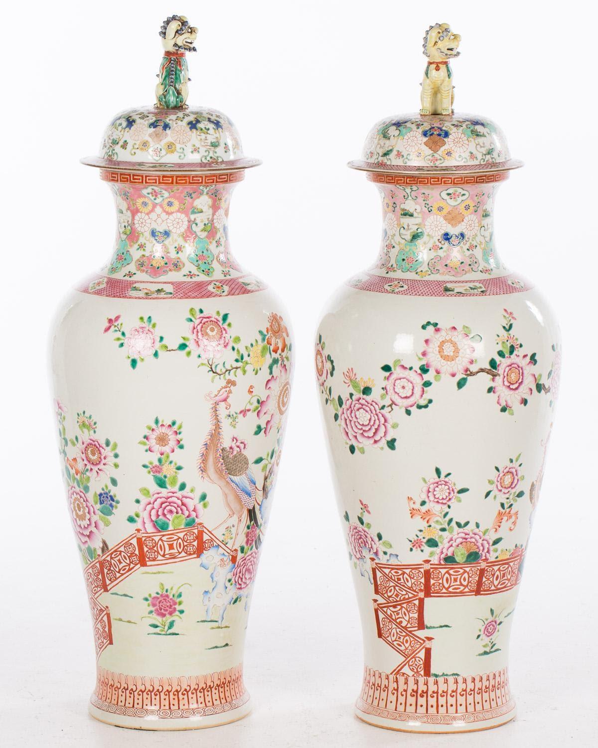 Large pair of circa 1900 Famille rose decorated porcelain covered vases, each decorated with fence, large flowering trees, landscapes within cartouches and lids with fu dog finials.