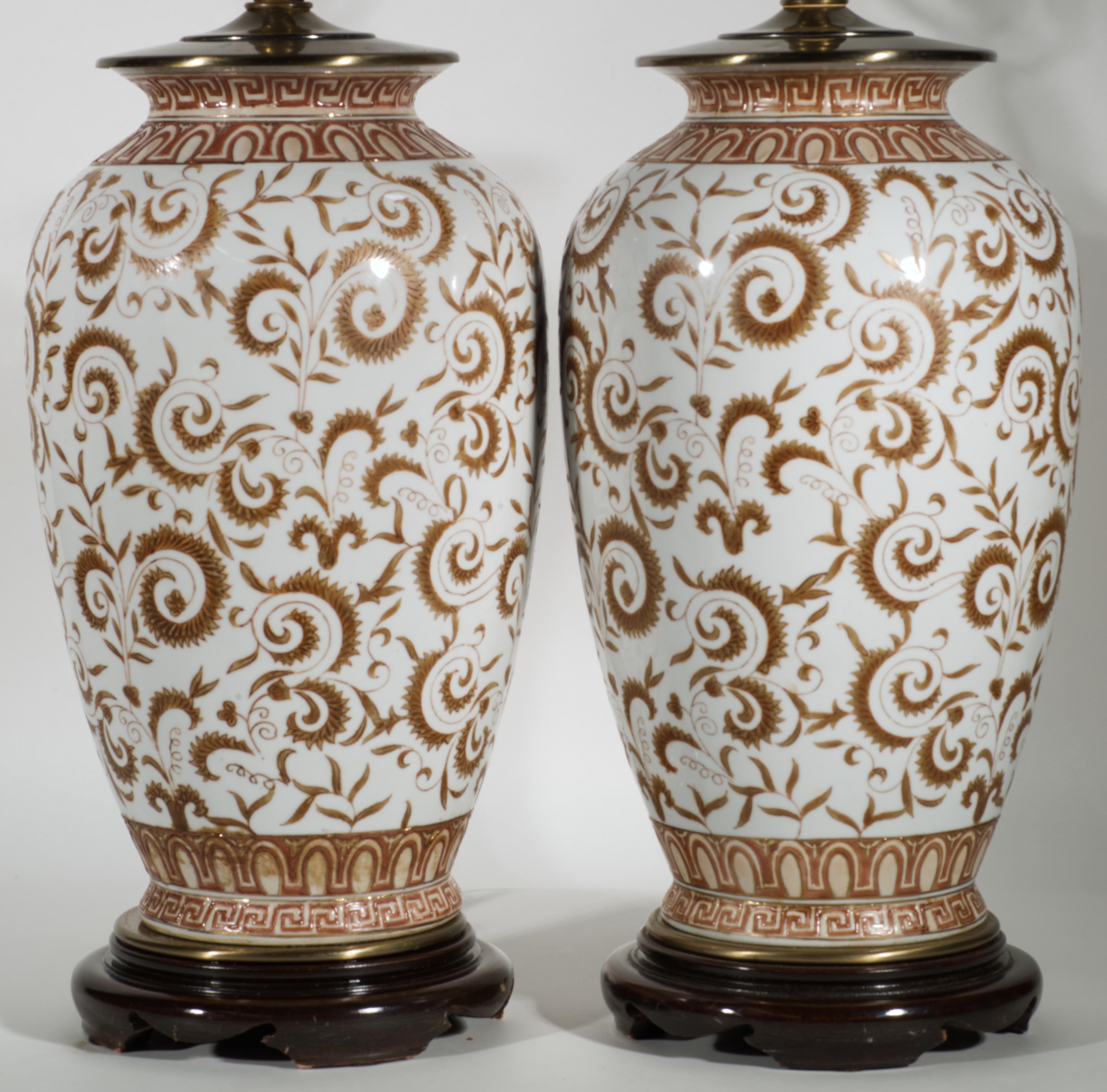 Vintage pair of large chinoiserie style urn or jar table lamps is mounted on round brass and carved wood bases and topped with fine brass fittings and substantial ornate brass finials. Classic porcelain or ceramic urn shaped bodies are decorated