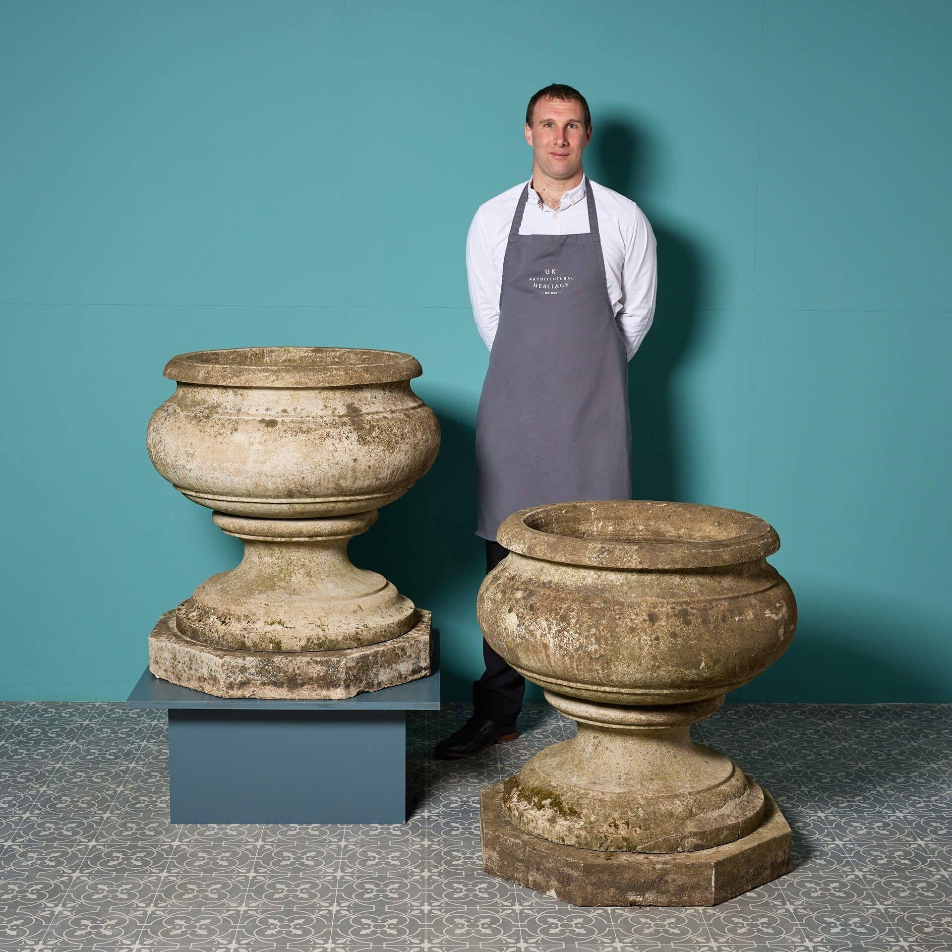 A pair of large reclaimed and beautifully weathered Victorian style scroll pots, robustly cast in composition stone that resembles a light Portland limestone.
 
In a substantial unusual scale, this planter features a naturally weathered finish which