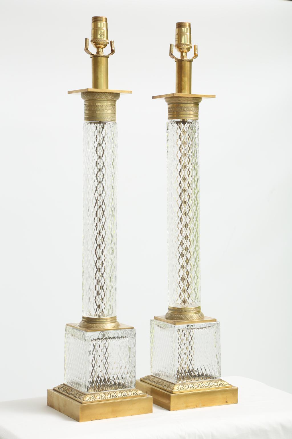 Pair of large scale table lamps, each a diamond-pattern cut glass column, with chased capital and foot of gilt bronze, on matching glass plinth, upon bronze doré base, decorated with classical palmette motifs. 

Stock ID: D2183