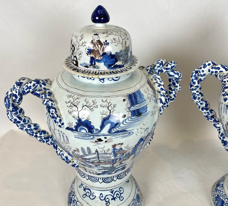 A pair of large and impressive mid-19th c. Delft lidded urns decorated throughout in a pallette of blues and browns with Chinoiserie scenes and beautifully twisted handles.
