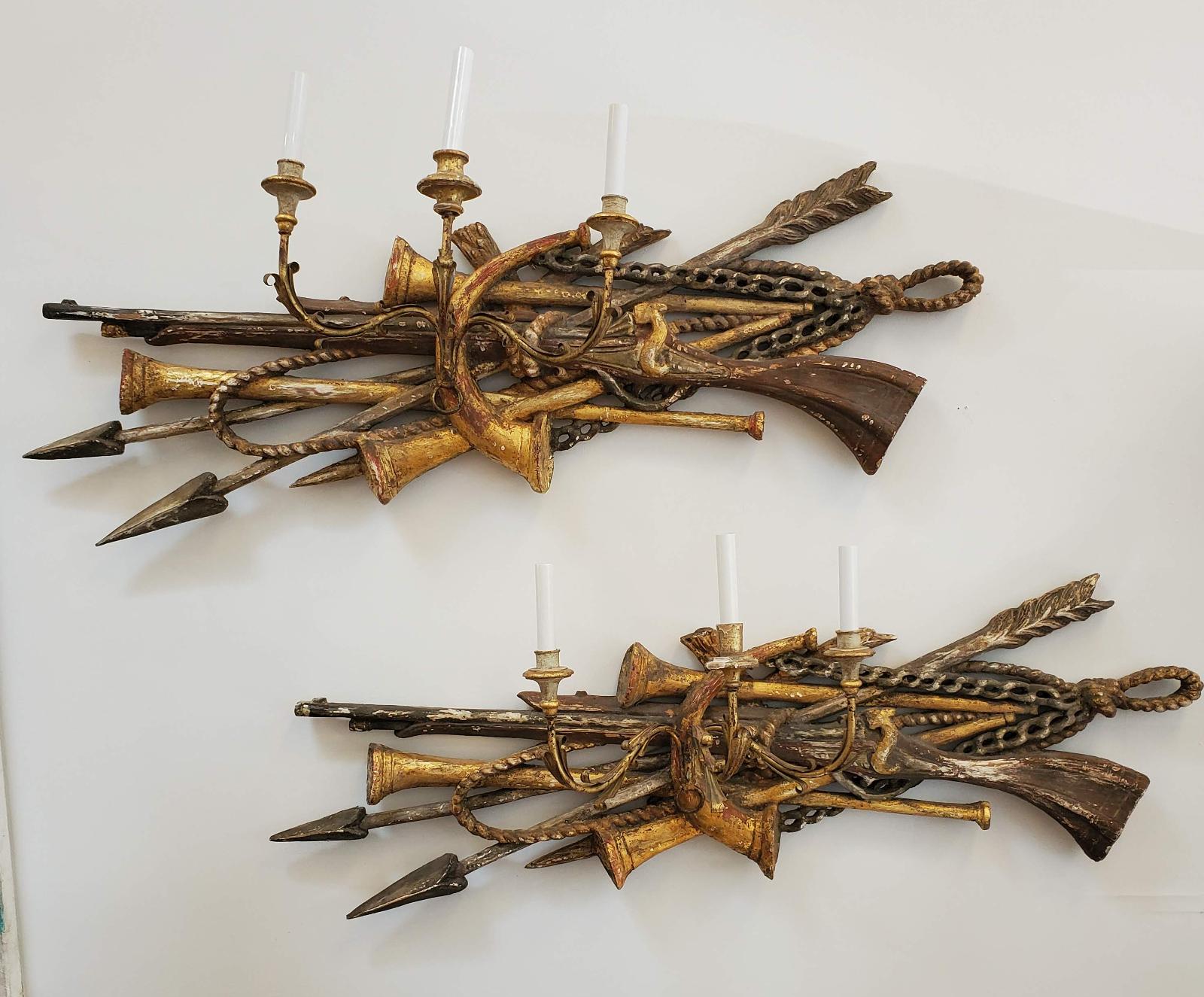 Extraordinary pair of Louis XVI style carved gilded wall sconces. Unusual large proportions. Beautifully carved detail depicting rifles, swords, hunting horns, spears, rope and chain. Each painted and gilded with three candle arms and electrified