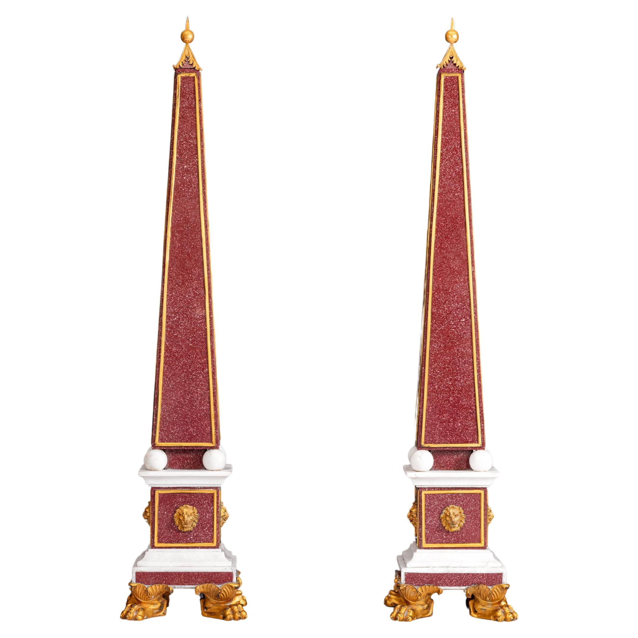 Exceptionnelle paire d'Obélisques en Porphyre, marbre et bronze doré, de forme typique surmontés d'un fleuron en fonte foliacée, reposant sur un socle à panneaux orné de masques de lion et sur une base carrée à gradins, sur des pieds en patte d'oie