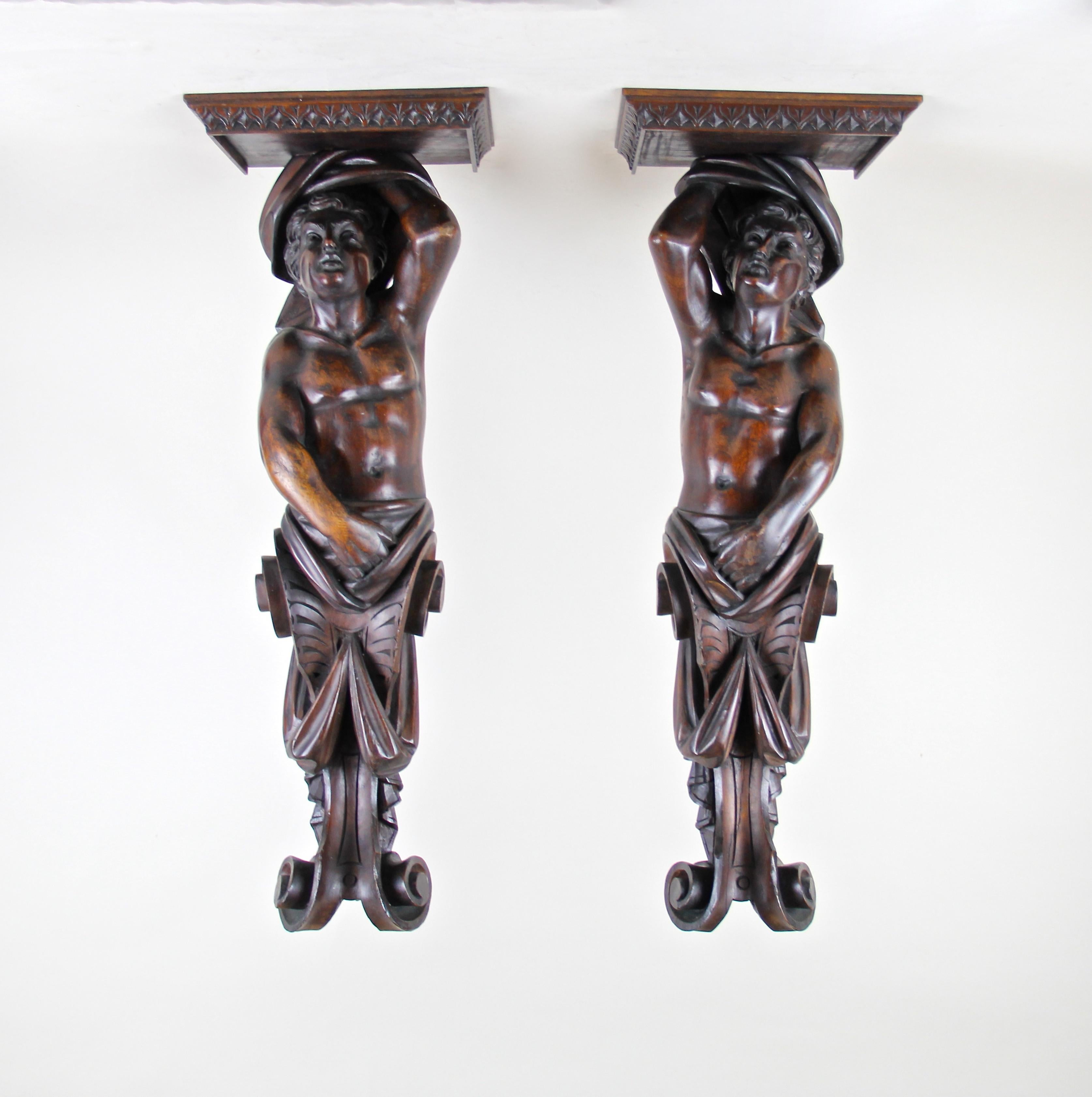Unusual pair of large figural wall consoles from Austria, circa 1870. By showing real craftsmanship, this fantastic pair was hand carved out of solid nut wood depicting two young athletic men carrying the top plate of these rare wall console tables.