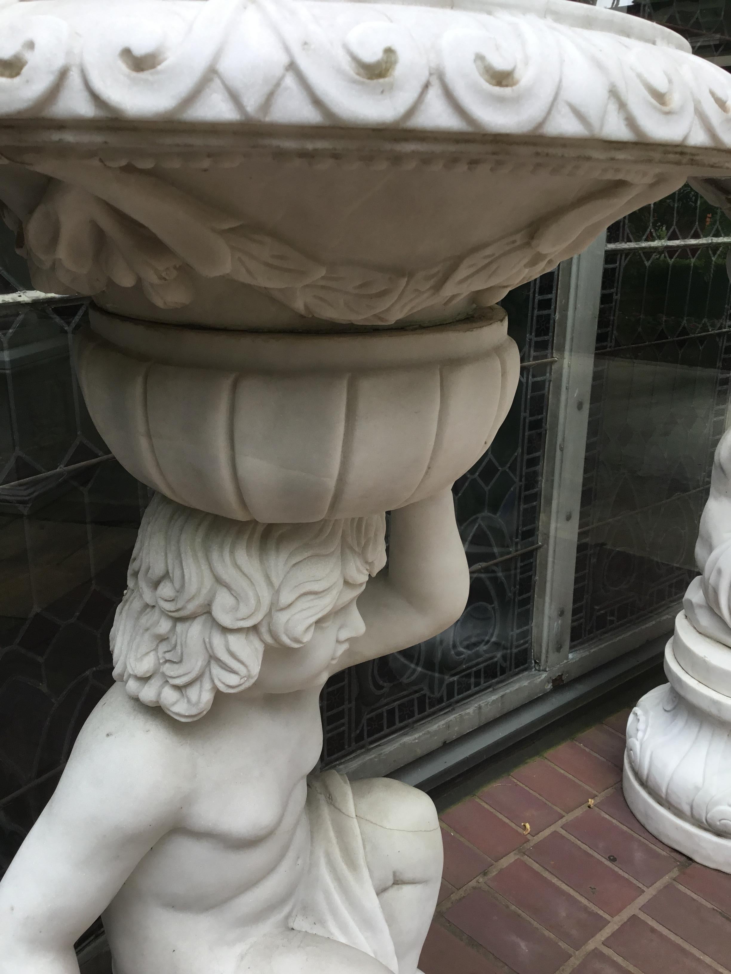 Pair of putti holding a carved marble bowl over their heads. All carved
marble. The figures slightly facing each other. Hole in the bottom of the
planter for drainage.