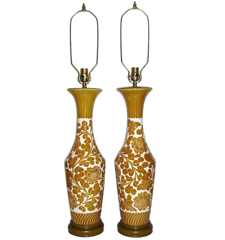 A pair of French circa late 1940s glazed porcelain table lamps with stylized floral/foliage decoration and wooden bases.

Measurements:
Height of body 25.5