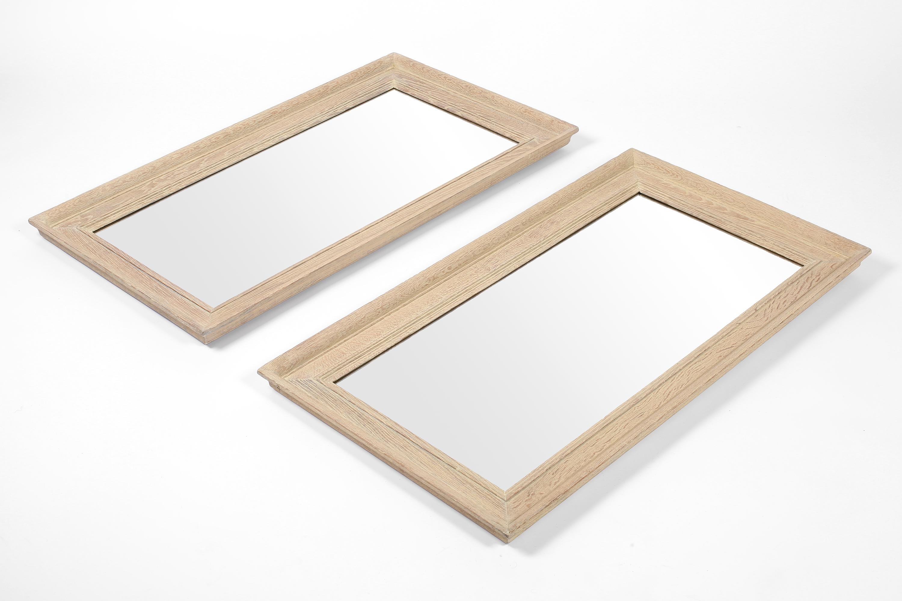 Paire de grands miroirs chic en chêne chaulé avec des cadres profondément sculptés, à la manière de Jean-Michel Franks. Équipé de nouvelles plaques de miroir et de chaînes de suspension. Français, c. 1940s.