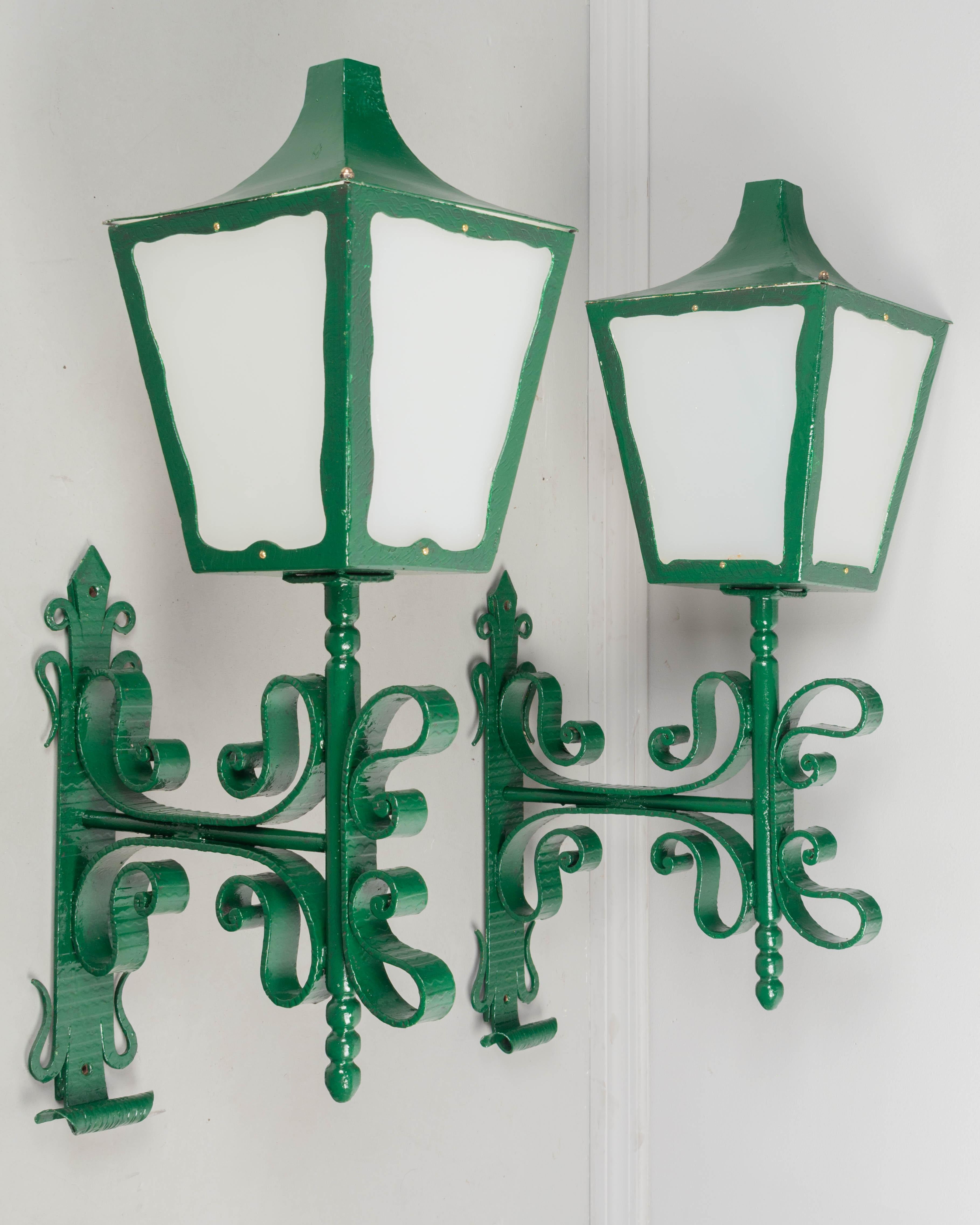 A pair of large scale architectural wall lanterns with decorative wrought iron brackets. Newly painted green with  opaque plexiglass panes. Rewired and in working condition. Circa 1950s.
Dimensions: 38