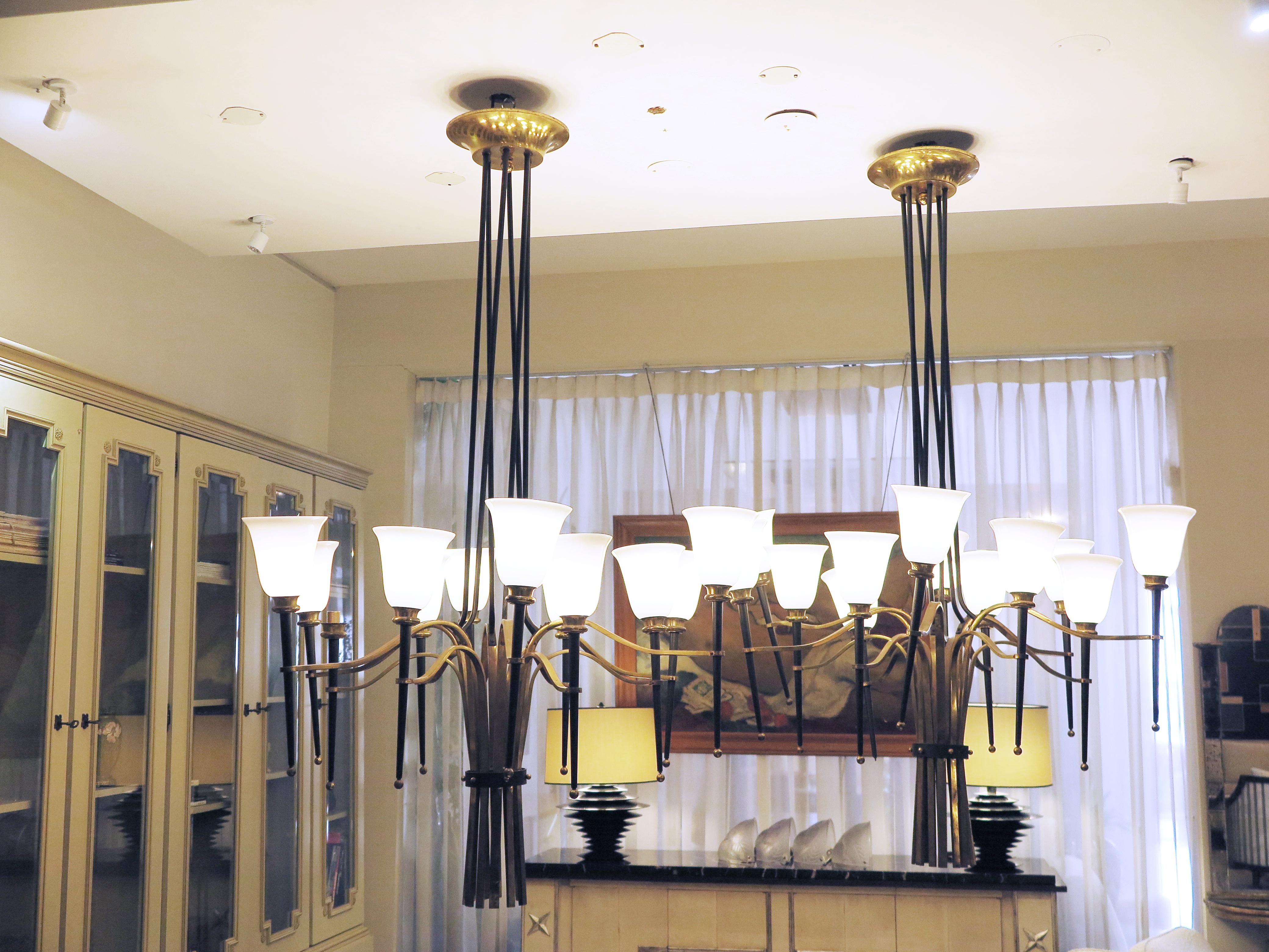 Pair of large Blackened Bronzed and brass chandeliers in there style of Gilbert Poillerat. The multi blackened center stems support 12 curved brass arms with opaline tulip shades. Sold as a pair.
