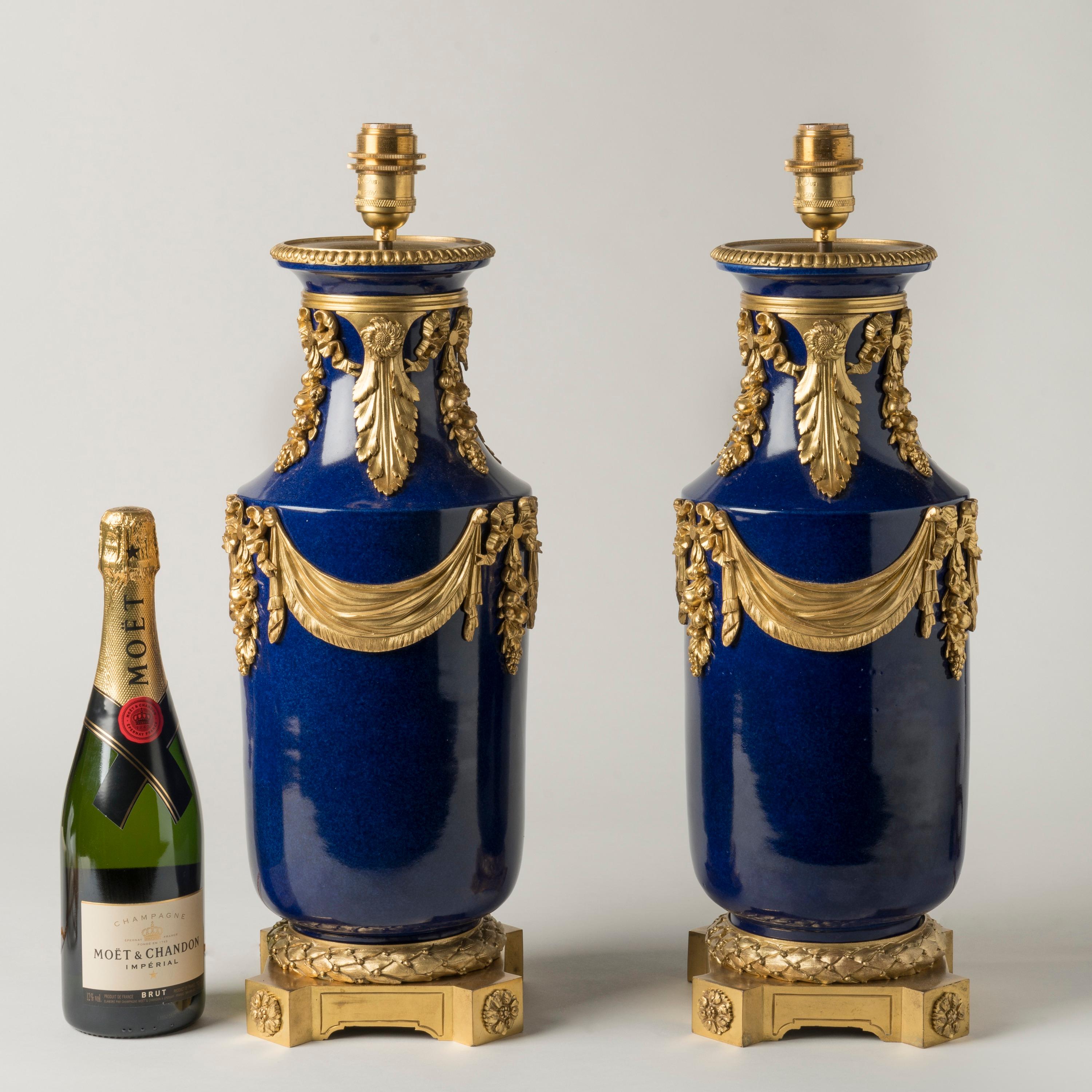 A Pair of Ormolu-Mounted Blue Porcelain Lamps
In the Louis XVI Style

The cobalt blue porcelain vases tastefully mounted with gilt bronze draped swags, ribbon-tied bunches of fruit, and acanthus-leaves, the bases also of ormolu, with everted corners