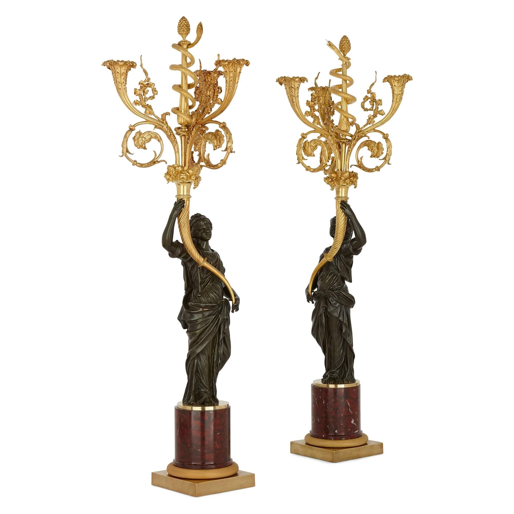 This impressive pair of candelabra features two Classically modelled maidens, holding above their head an extravagant fruit-filled golden array, which each issue a trio of candle-branches with corolla nozzles, scrolled foliage and cockerel head