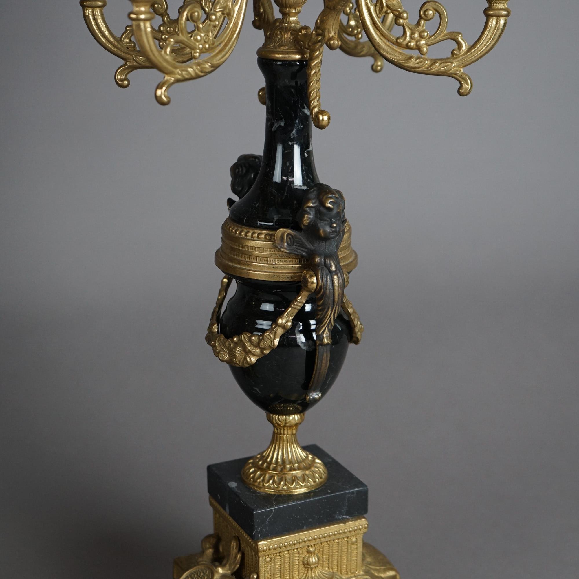 A pair of French Empire style candelabra offers gilt bronze and ebonized construction with scrolled foliate form arms terminating in candle sockets; ebonized base with cherub masks and gilt bronze footed mounts, 20thC

Measures - 24.5
