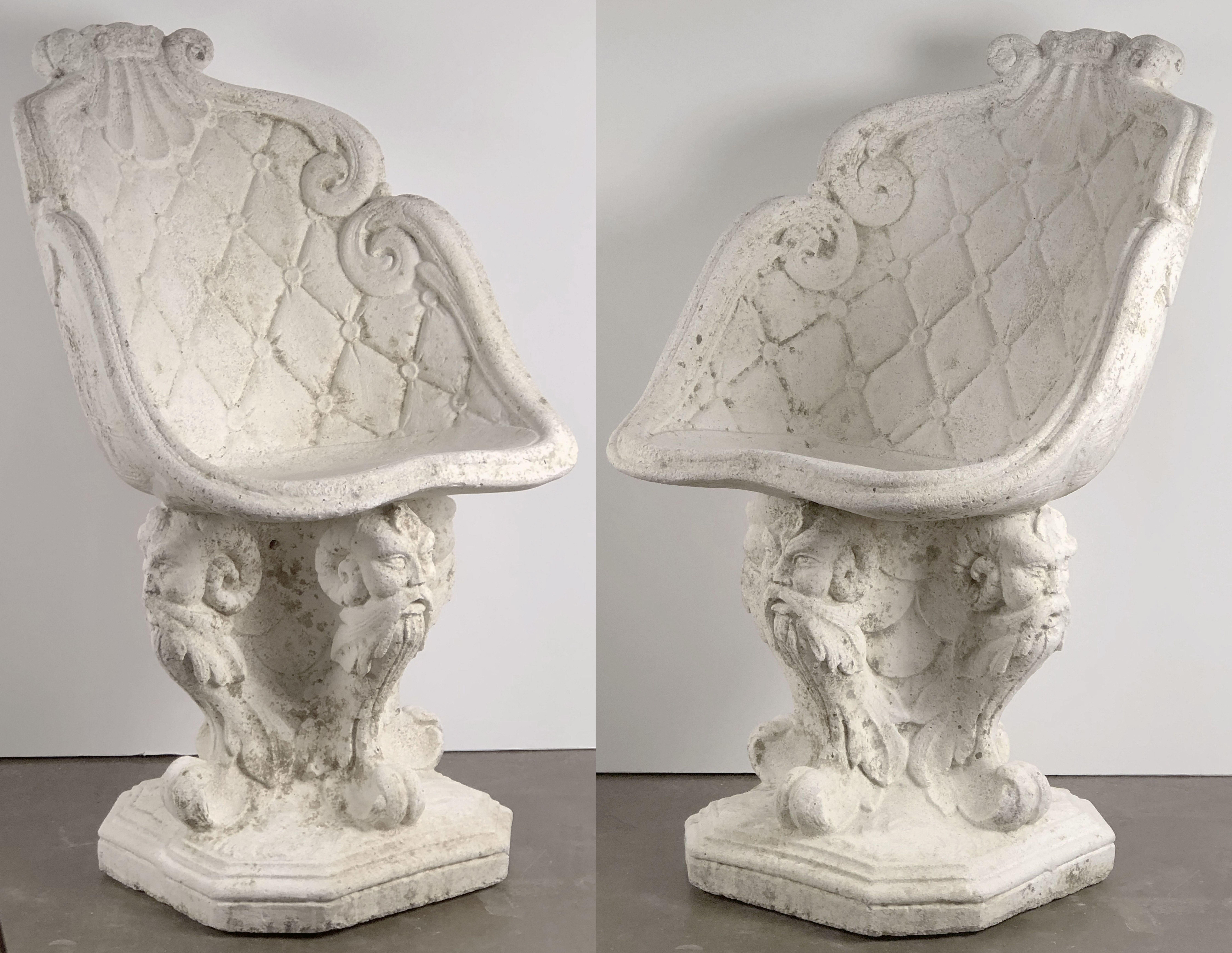 A fine pair of large Italian garden chairs of composition stone, each chair featuring a back and seat with a shell and scroll design, over a pedestal base with four Gothic figural heads.

Dimensions are H 34 3/4 inches x W 20 1/2 inches x D 22 1/2