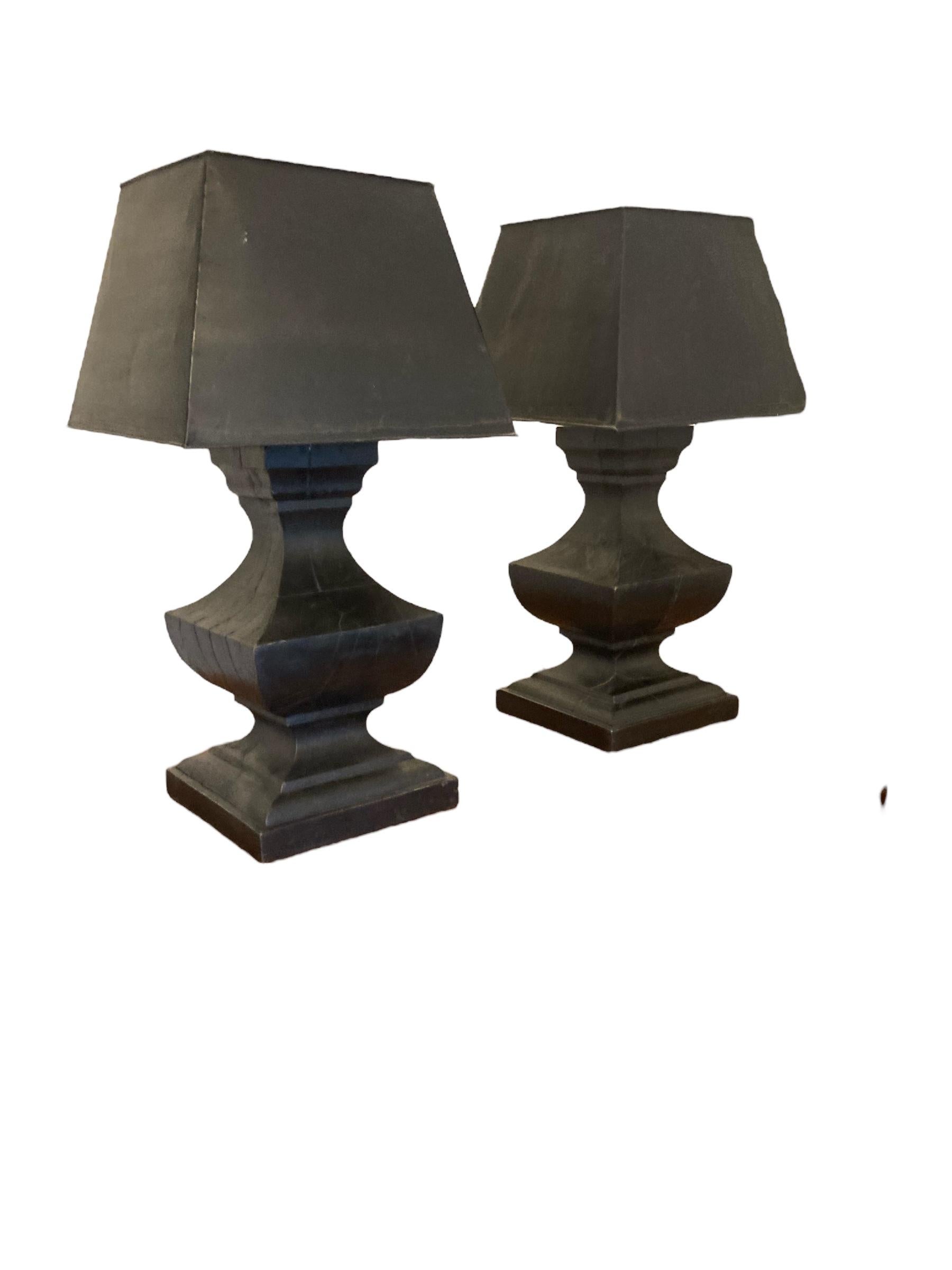 A Pair of Large French Hand Carved Table Lamps, Ebonsied Wood with Black Metal Shades. Early 20th Century. These elegant lamps, mounted on sturdy wooden bases, seamlessly combines industrial charm with rustic appeal. Their sleek design and