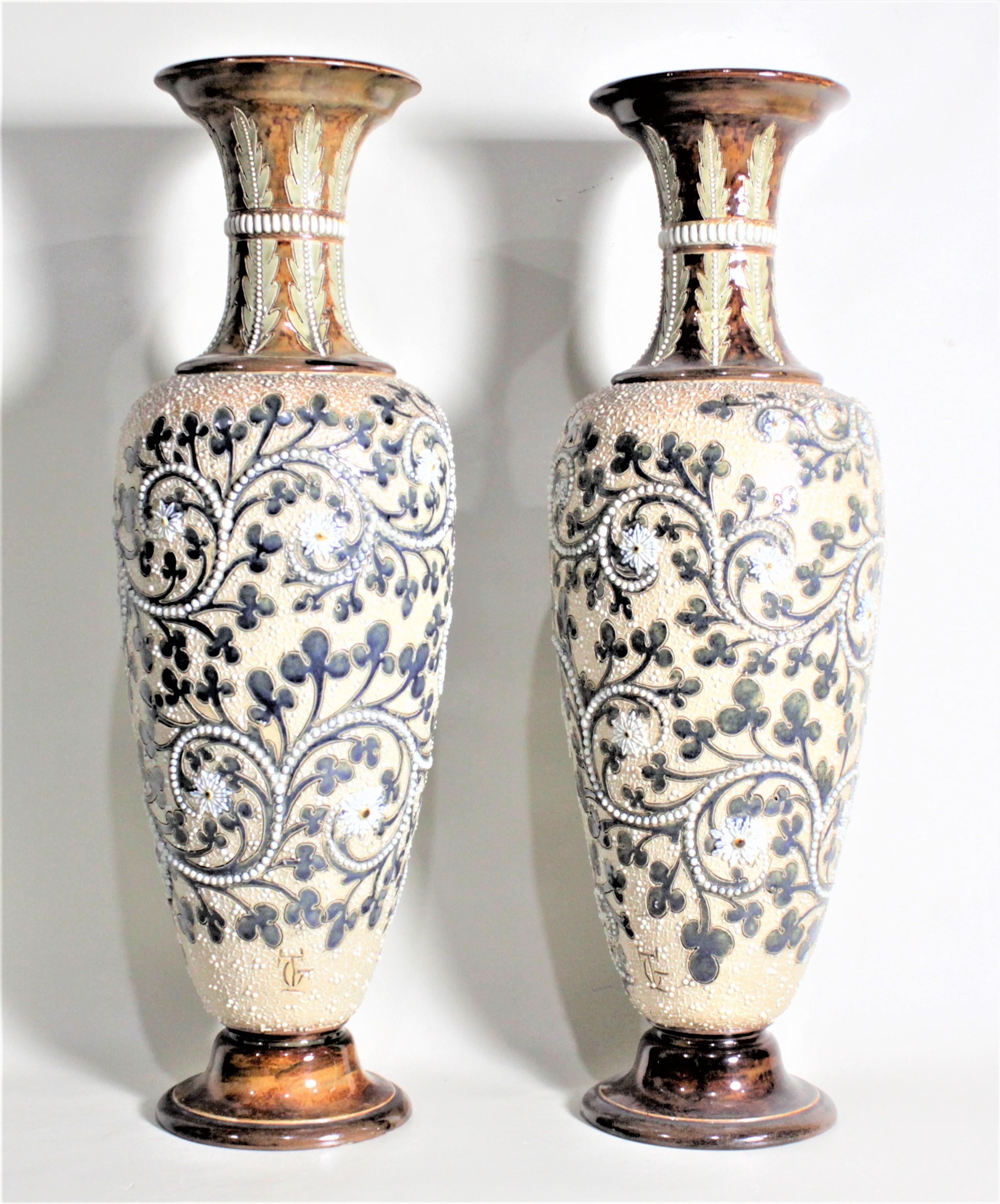 This pair of antique stoneware vases were done by the renowned potter, George Tinworth for the Doulton Lambeth factory of England in approximately 1880 in the period Victorian style. The vases are done with a deep cream ground with elaborate beaded