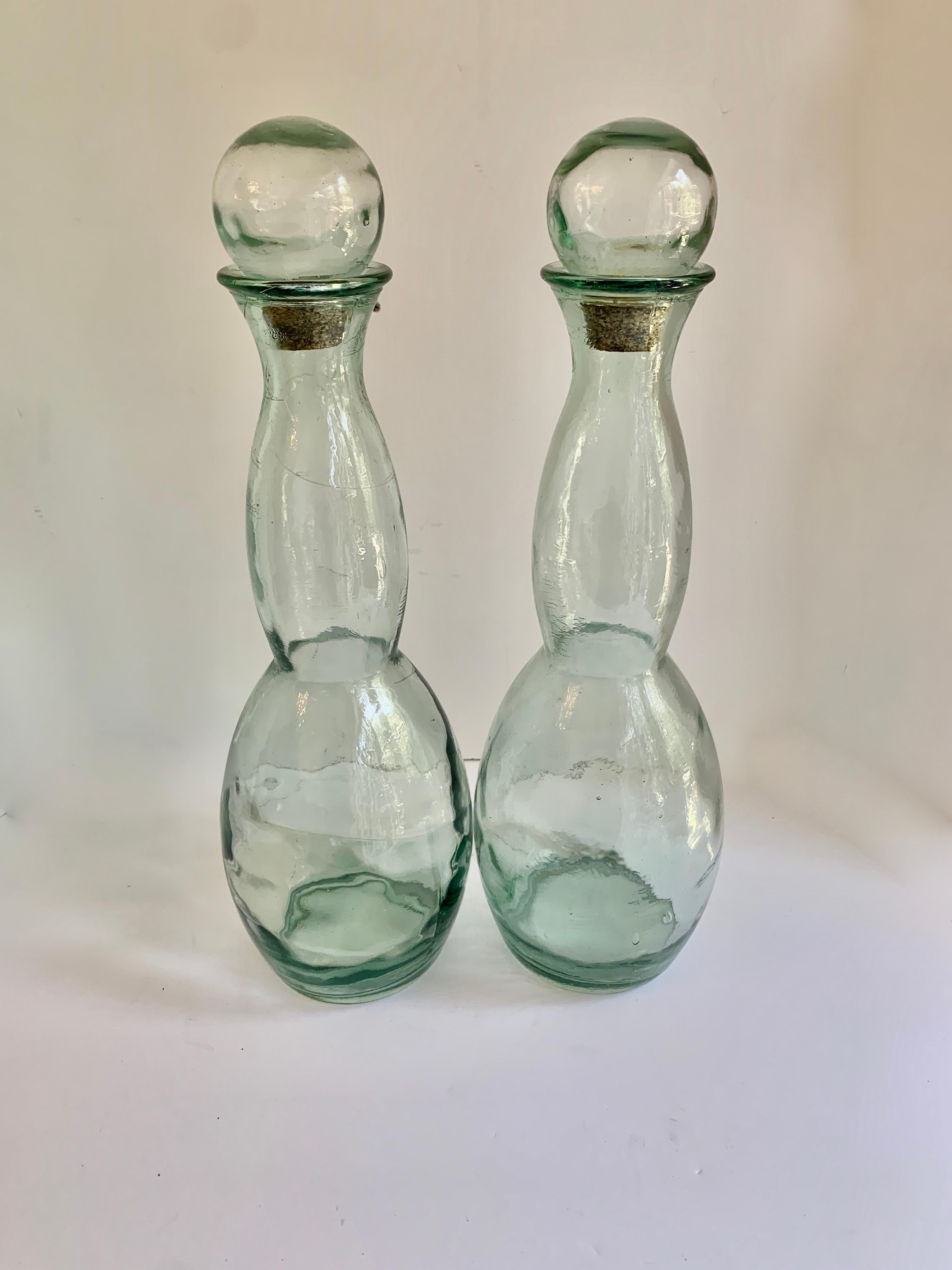 A pair of large hour glass shaped glass jars with Ball finial cork tops. A perfect companion to flank a large shelf or decorative wall in a utilitarian space. While wonderfully suited as a decorative pair, could certainly serve as a practical