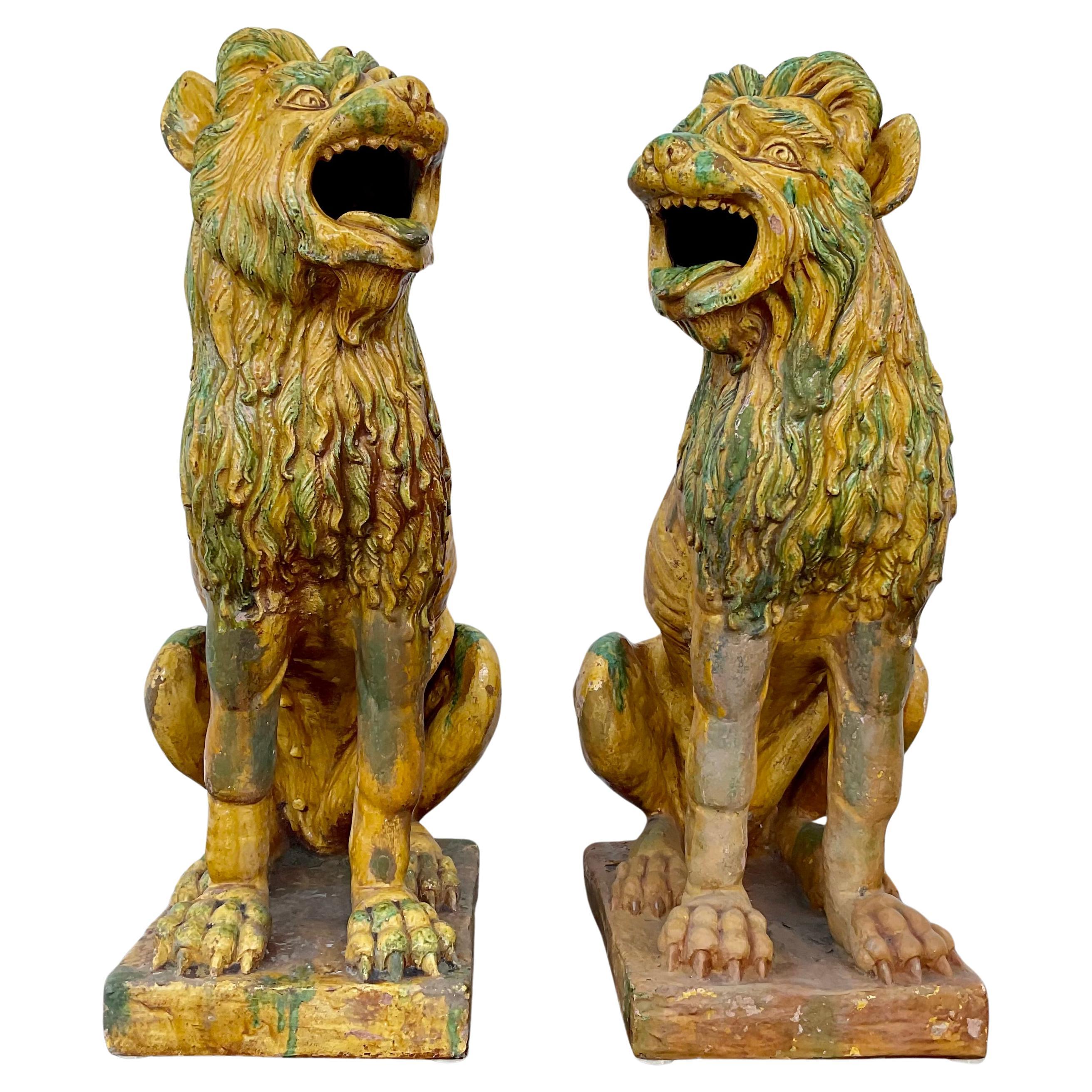 Extraordinaire paire de statuettes de chiens ou de lions en terre cuite décorative, vers le début du 20e siècle. Glacés en vert, jaune et rouge avec de légères différences indiquant qu'ils sont faits à la main. Utilisés pour garder l'entrée des