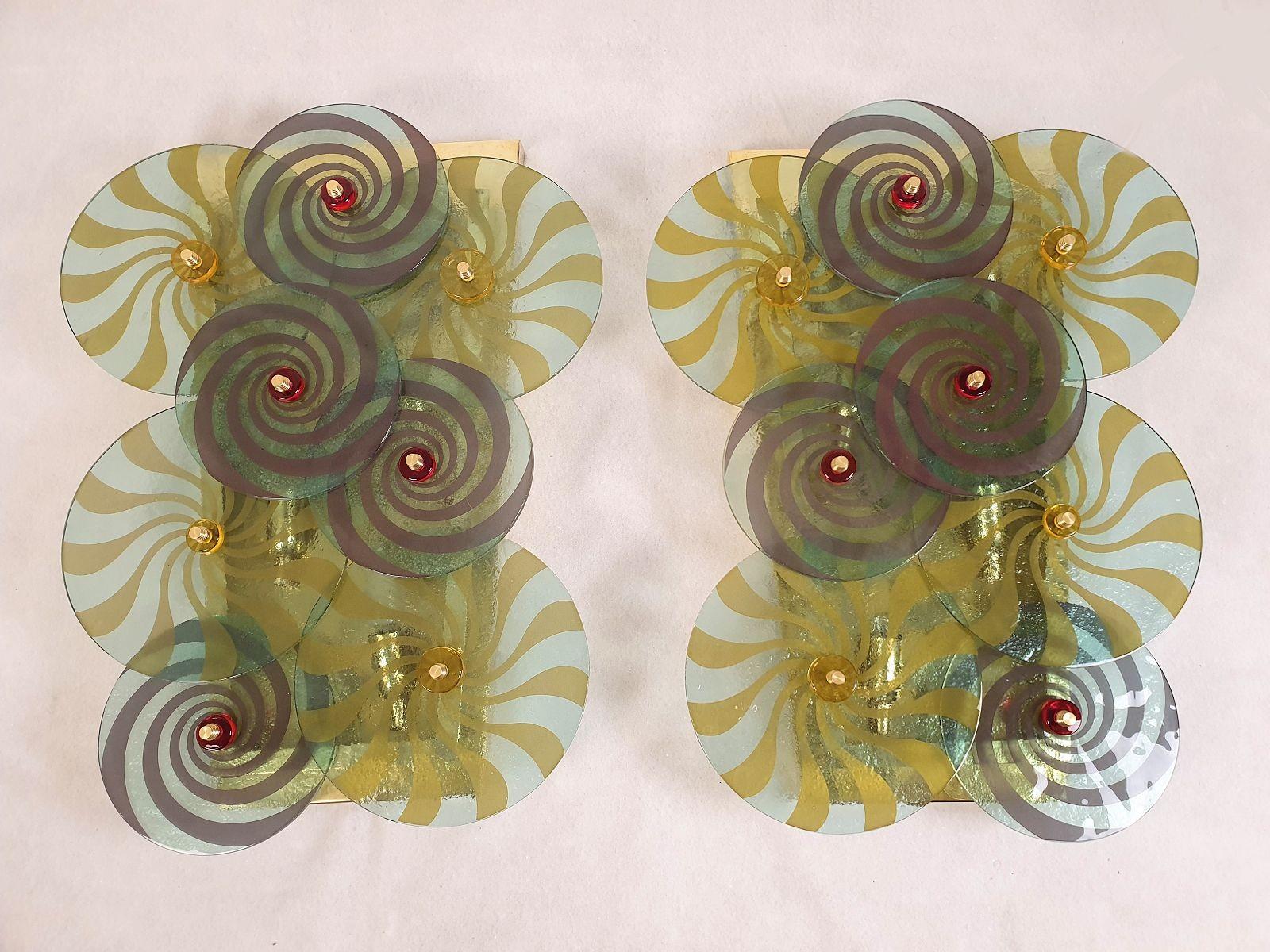 Pair of large Murano glass discs wall sconces, attributed to Vistosi, Italy 1970s.
The mid century modern sconces are made of polished brass mounts and green Murano glass discs with handmade decor.
The Murano glass discs are very unique.
Each