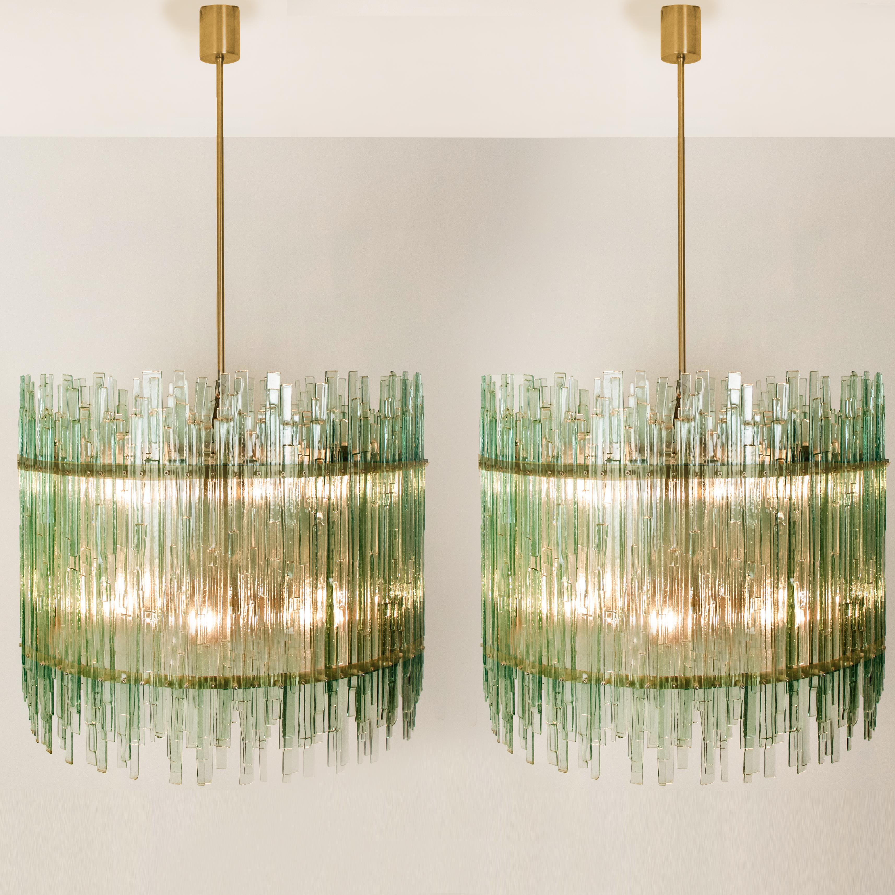 This model is a nod to the 1960s, yet has a distinctly modern allure.
Several stunning sea green hand blown Bullseye glass sheets are dangling on a massive brass frame. This unique chandeliers are not only functioning as a light source but also as