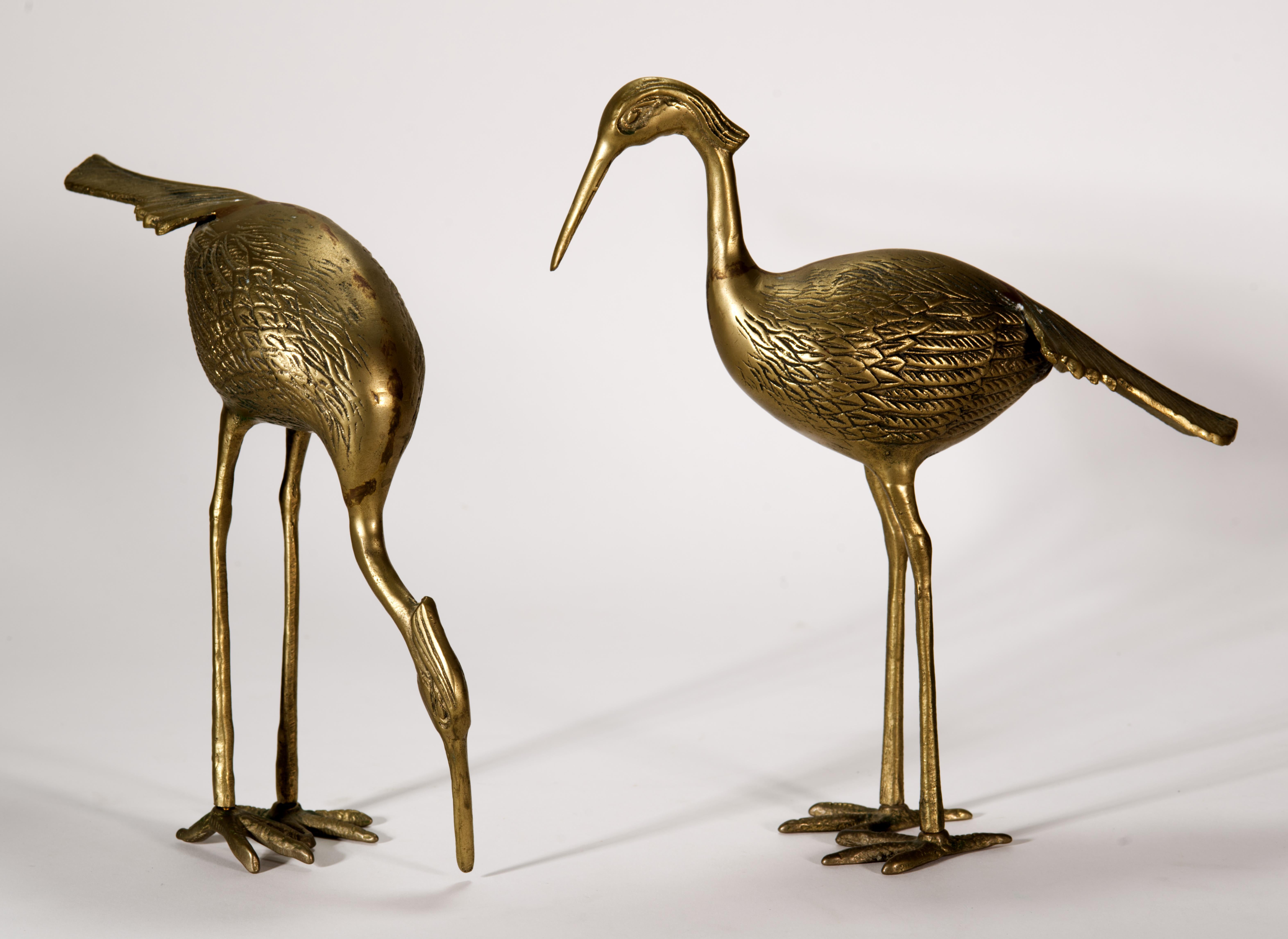  La coppia vintage di statuette di gru o aironi è realizzata in ottone con corpi scultorei e altamente dettagliati. Gli uccelli sono scolpiti in pose leggermente diverse, offrendo un ulteriore interesse visivo all'accoppiamento, con una gru in piedi