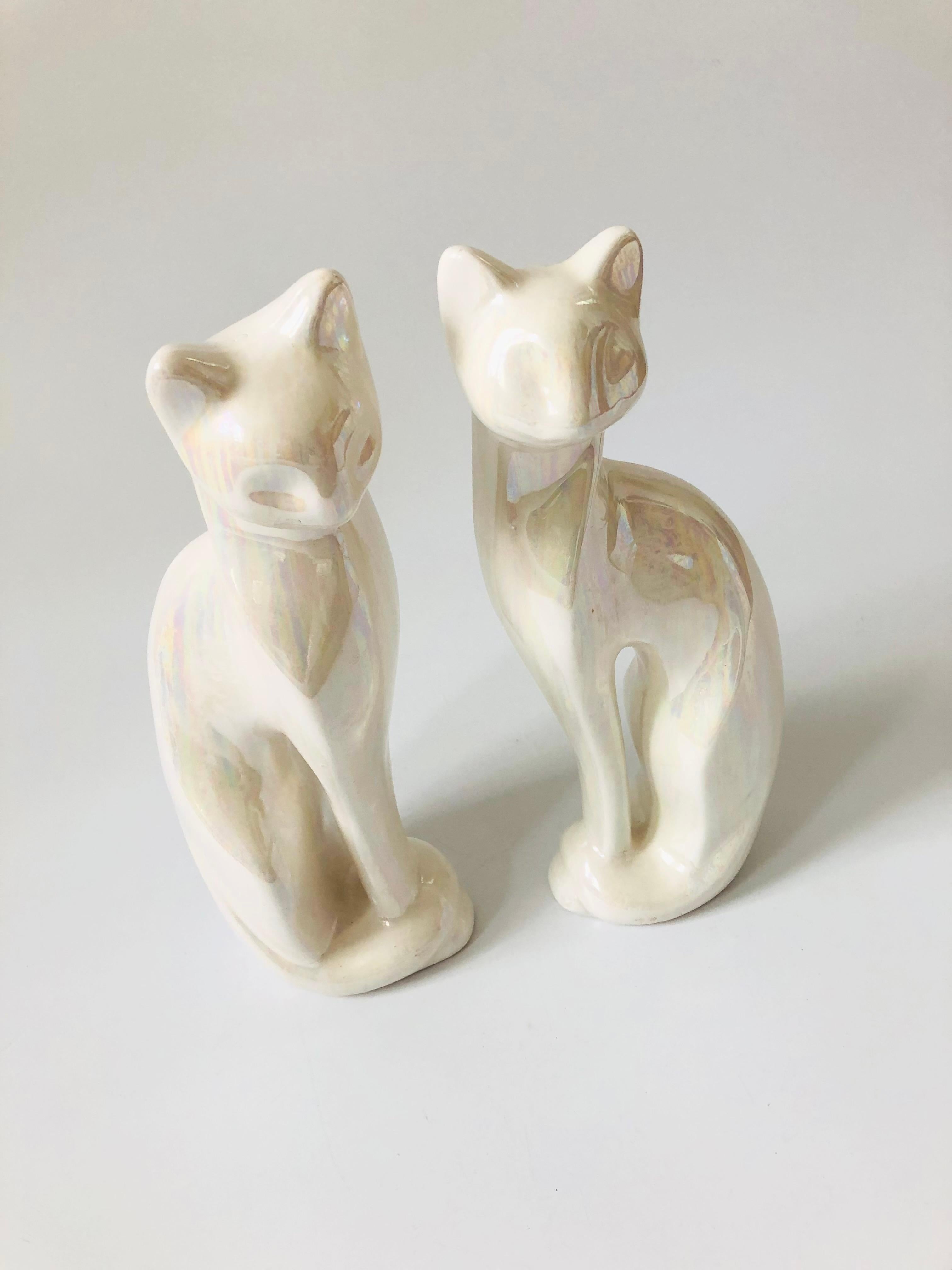 A pair of mid century ceramic cat sculptures, each finished in a glossy white iridescent glaze. Elegant pieces with great simplified stylized details to each cat's features. Please note, the cats are about the same size but not perfectly