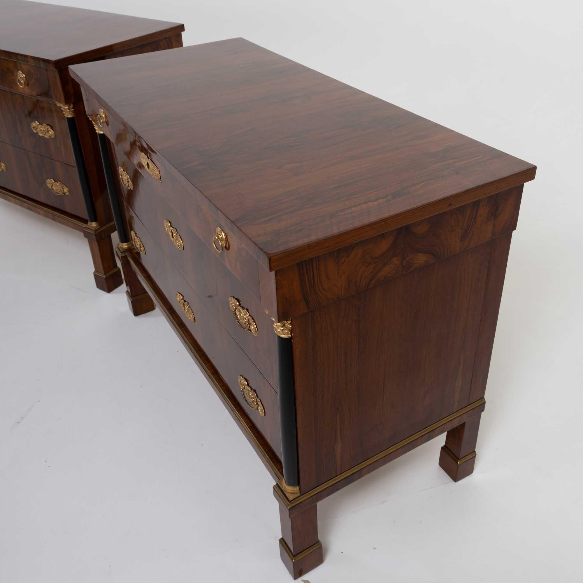 This impressive pair features three spacious drawers and stands on tall feet with gilded brass profiles. Each chest is flanked by ebonized columns with gilded bases and capitals, which support the narrower upper drawer. The chests are beautifully