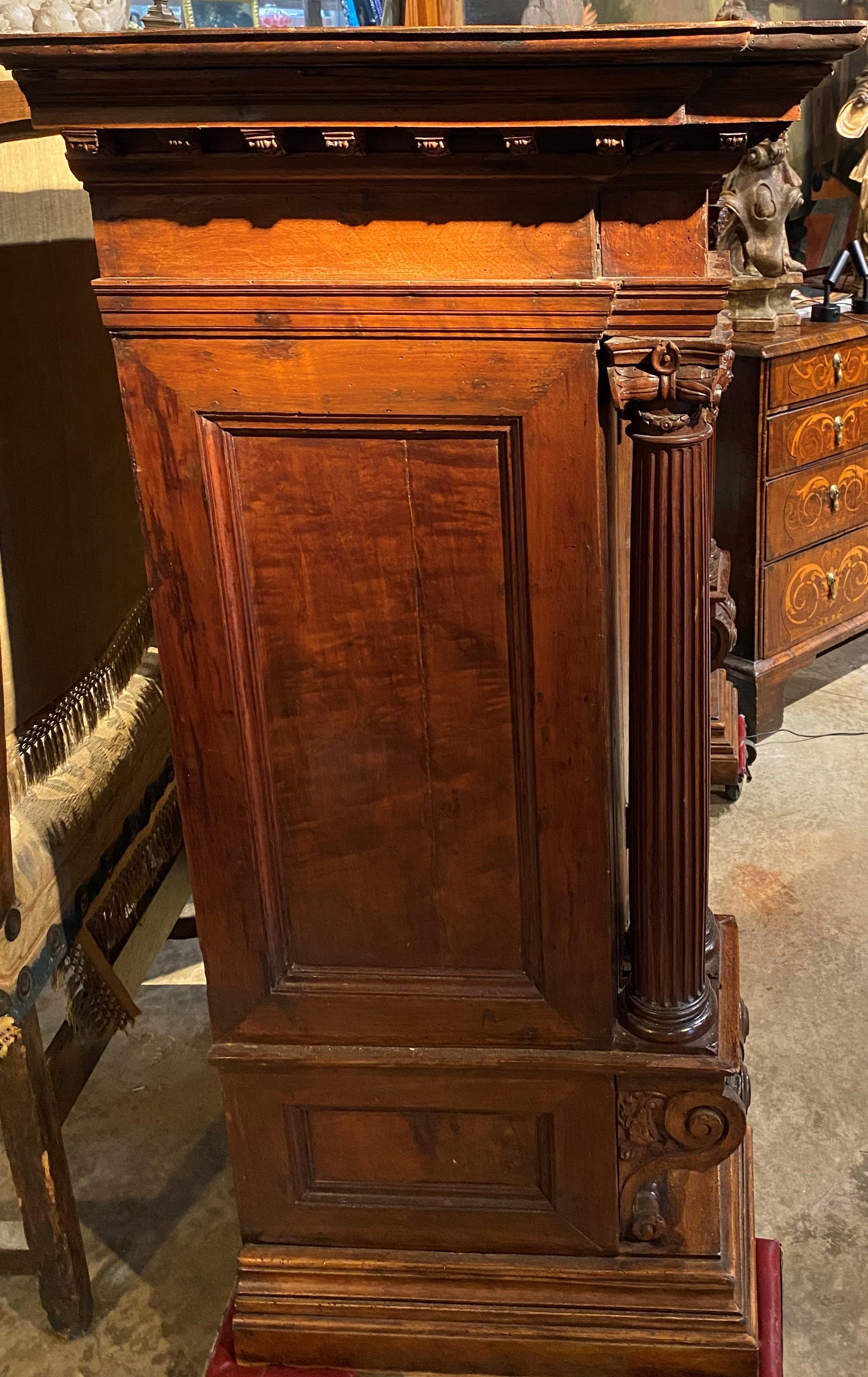 An impressive pair of large Neoclassical walnut architectural cabinets, each with a shaped top with molded edge accented with dentil molding surmounting a conforming case with two doors with original locking hardware, opening to a single interior