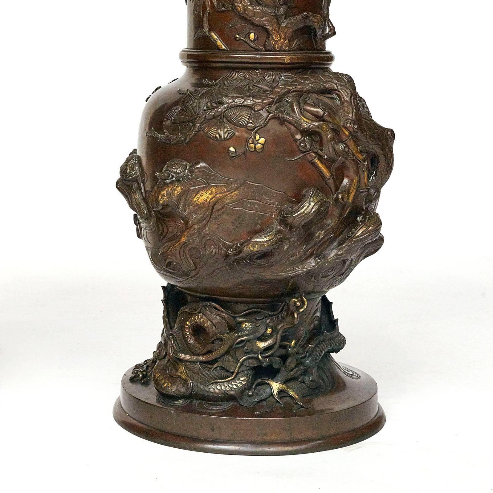A pair of unusual large Japanese cast bronze vases, Meiji period, 1860-1912. Patinated bronze with bronze highlights, the top lip with a Greek key frieze, the neck and body with cast branches, turtles, and birds, the lower part with a large dragon