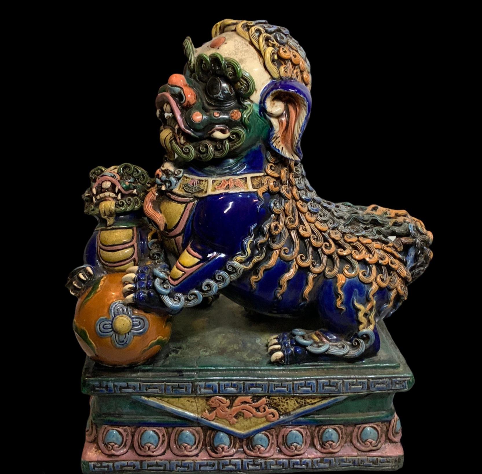 This is a pair of shiny colorful hand painted ceramic heavy Foo Dogs sculptures. One of them has a ball (male) and the other (female) shares the ball with a puppy foo dog. They  have big expressive black eyes and large dogtooth. Both of them are