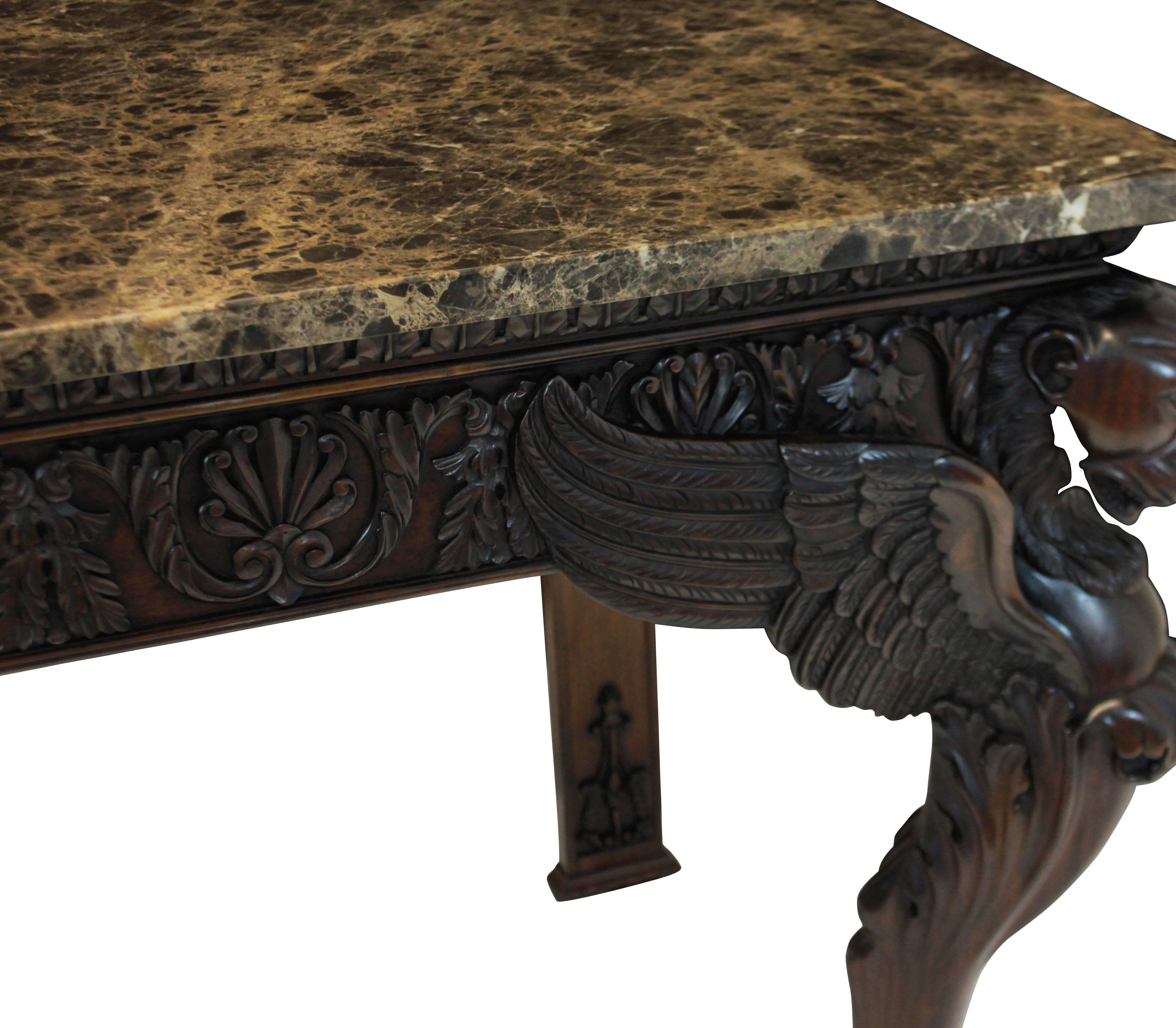 A pair of large English country house console tables of fine quality. Of beautifully carved mahogany in the early 18th century style, with winged beasts and intricately carved friezes with dark brown imperial marble tops.

  