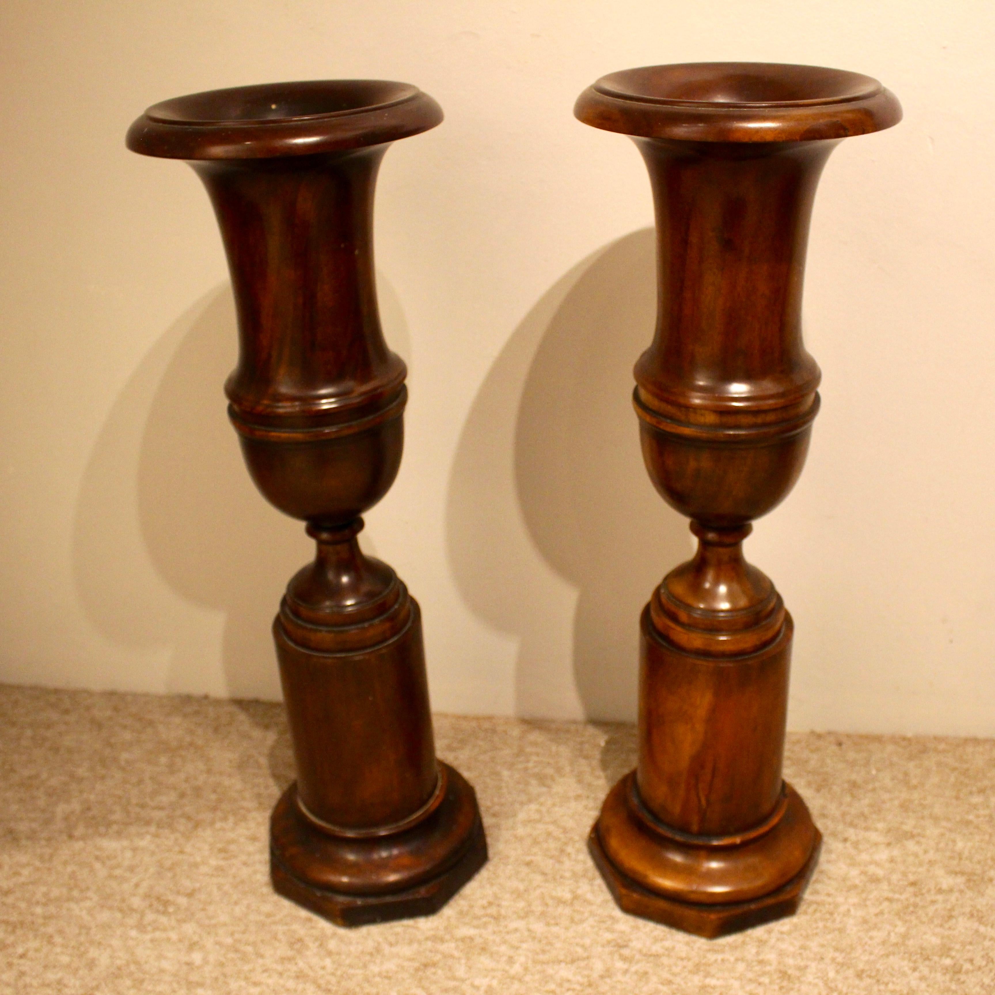 A lovely decorative pair of mahogany urns in the classical form. The Campana shaped upper section sits above a lower cylindrical base with an octagonal foot. Of good size and color. Would suit a modern or period interior.