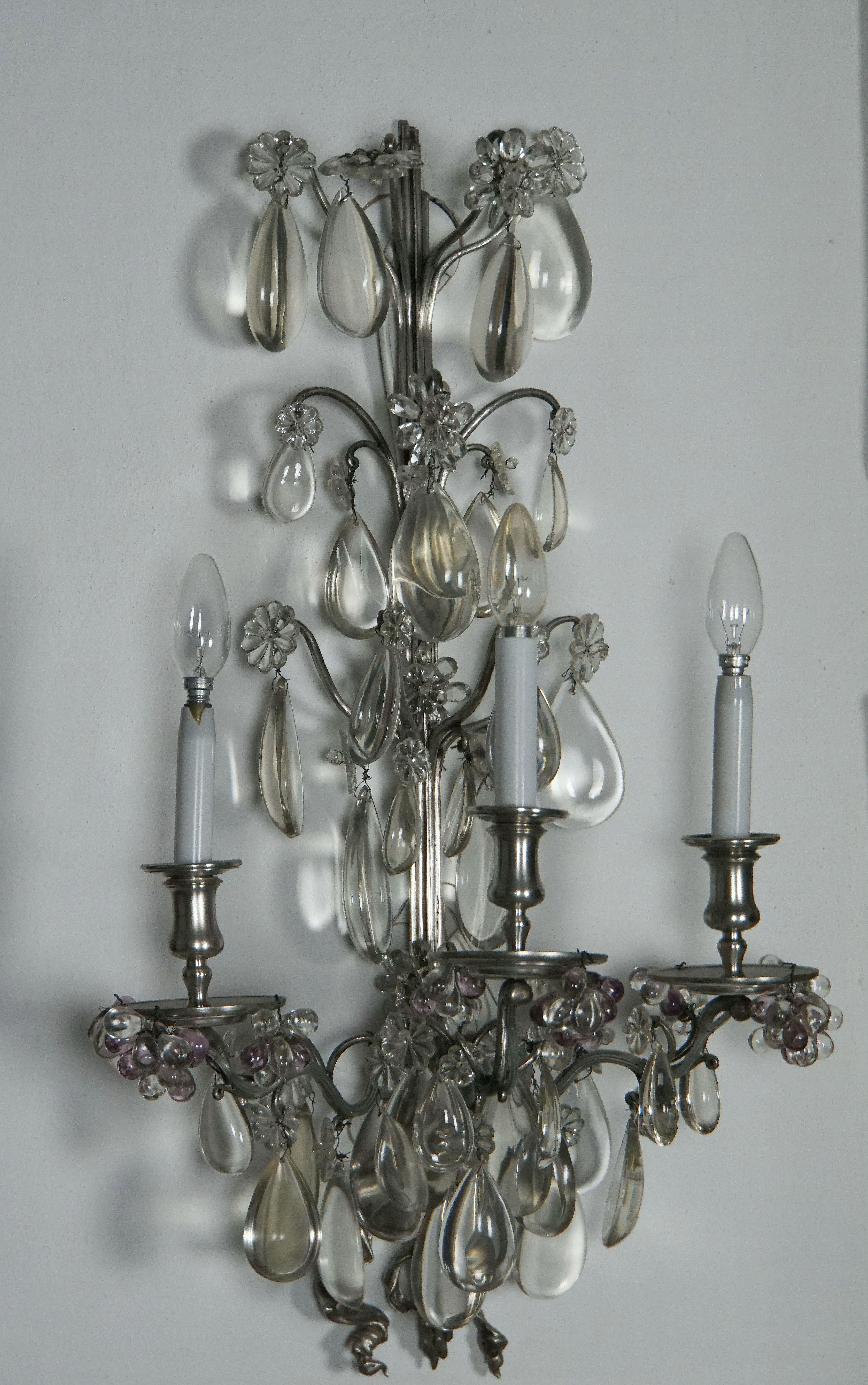 This pair of large Maison Baguès sconces are richly decorated with finest and large crystal drops. Each light features three arms in silver plated bronze and three chandelier bulbs. France, Paris, 1930.